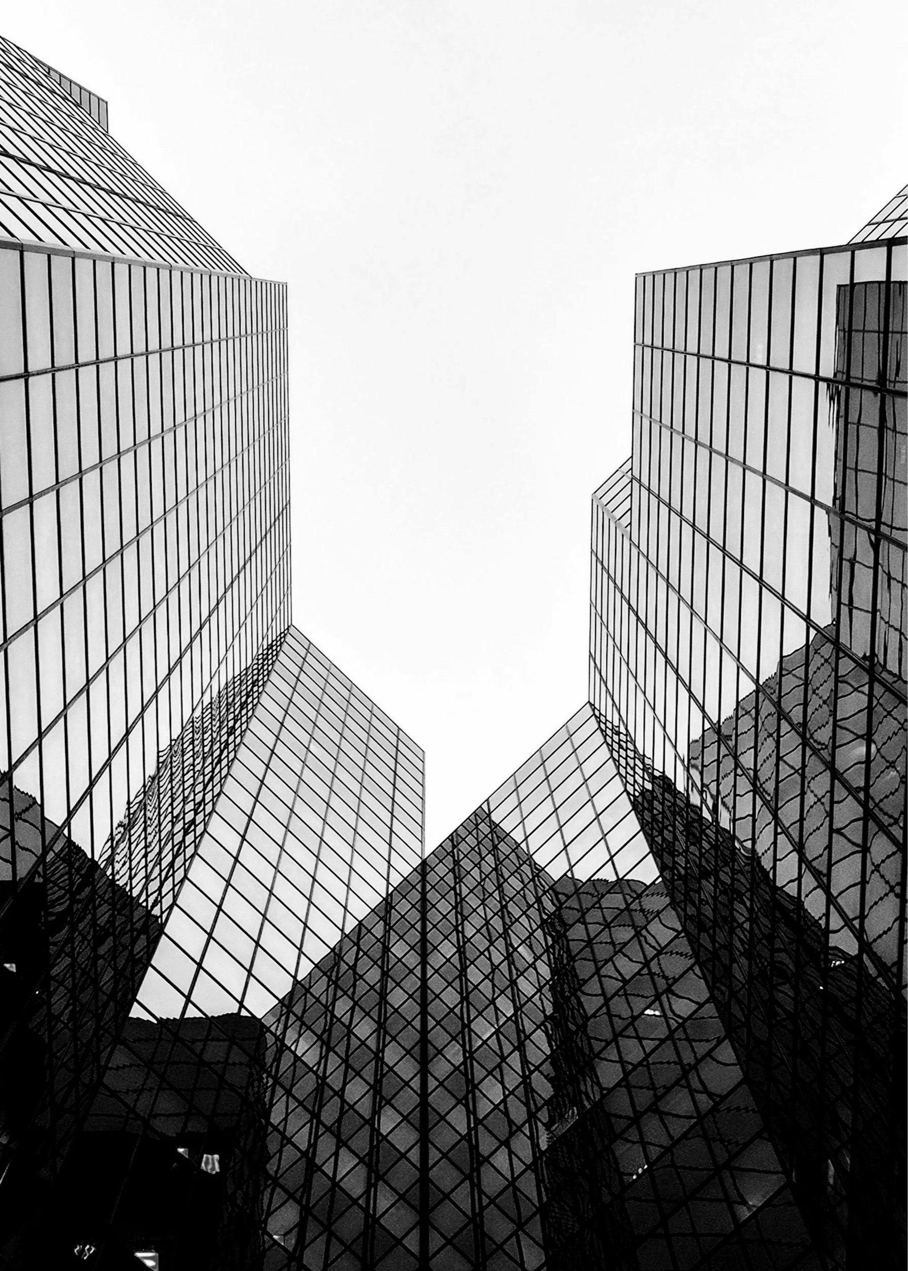 Looking up at modern glass skyscrapers from below, with reflective glass panels and geometric architecture.