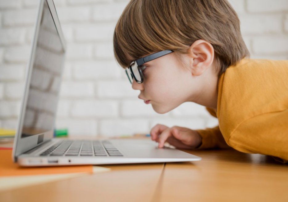 Child with glasses leaning over a laptop, appearing focused on the screen.