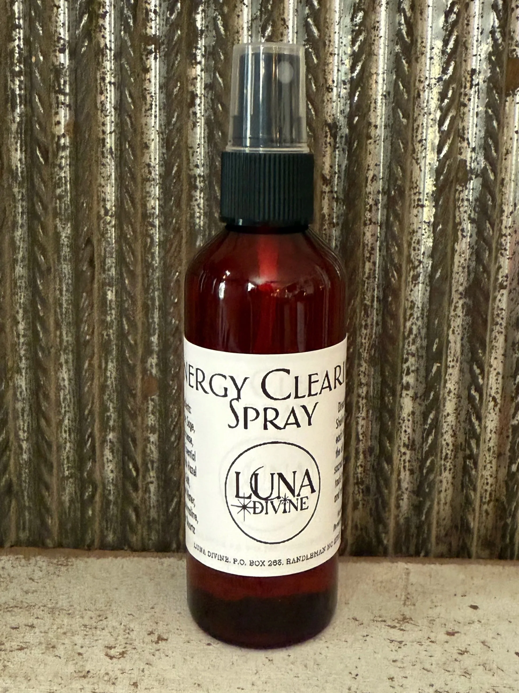 A brown spray bottle labeled "Energy Clear Spray" from Luna Divine, with a black spray nozzle, placed against a textured wooden background.