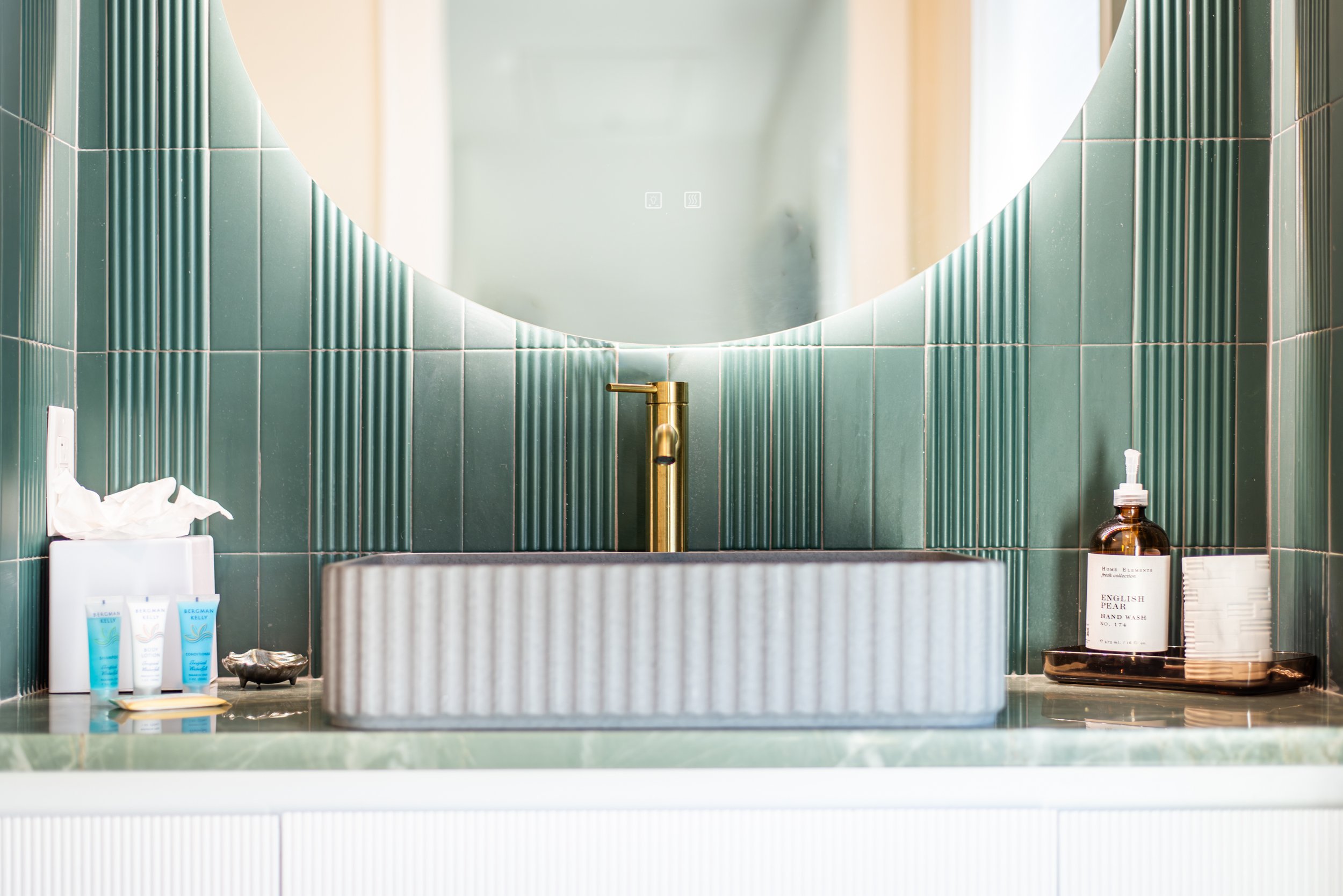 Bathroom with green tile vanity and circular mirror at Kate’s House, a Santa Rosa Beach vacation rental.