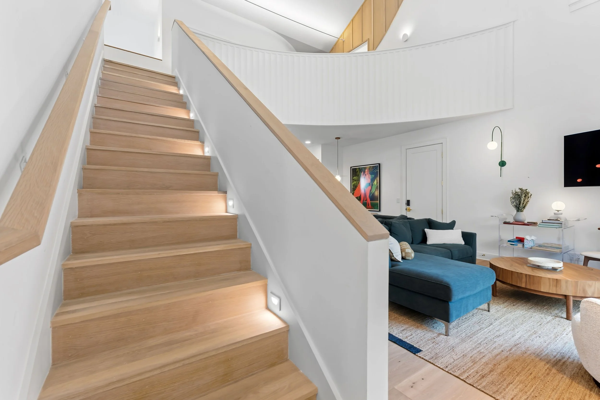 Grand stairway within the double-height living space at Kate’s House, leading to additional bedrooms on the upper level and showcasing the home’s open, architectural design.