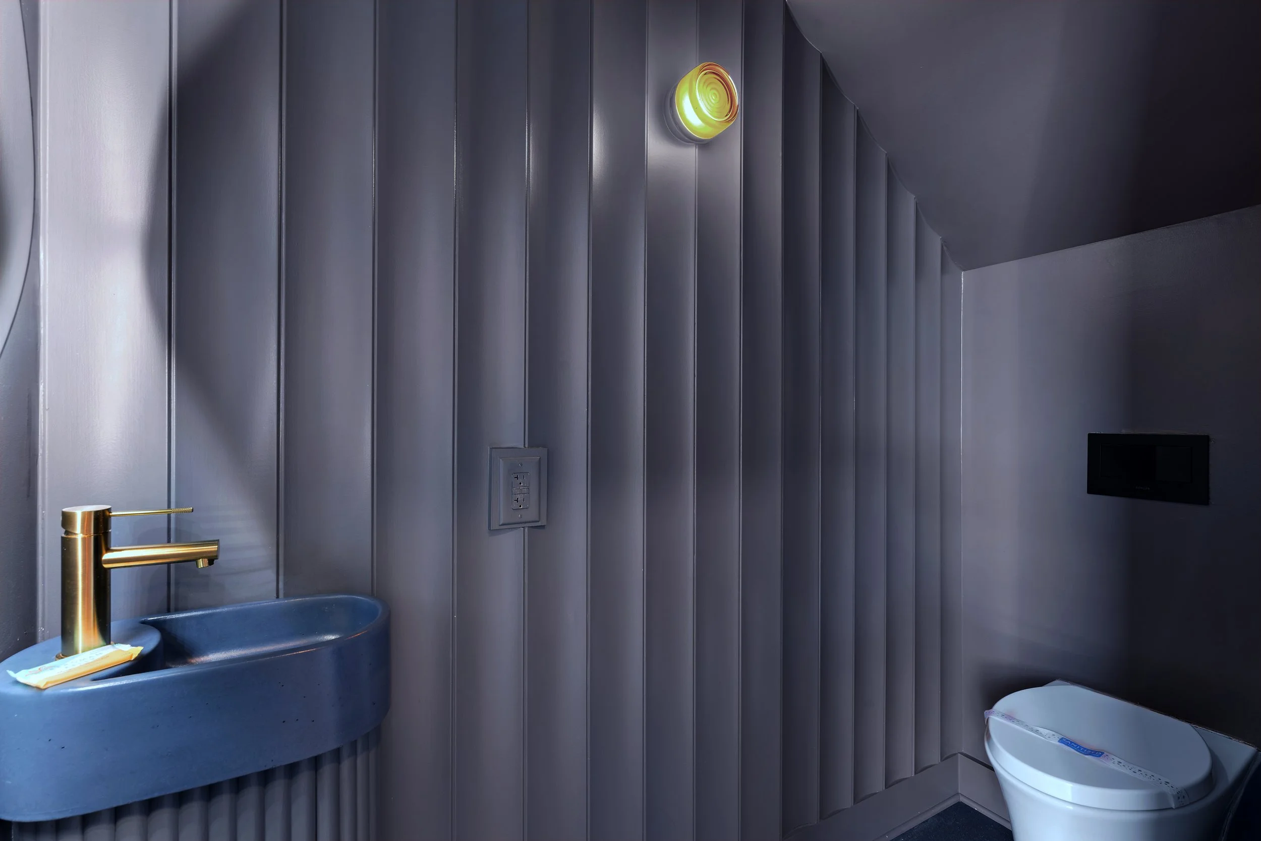 Modern powder bath with custom blue concrete sink, brass faucet, vertical shiplap, and wall-hung toilet.