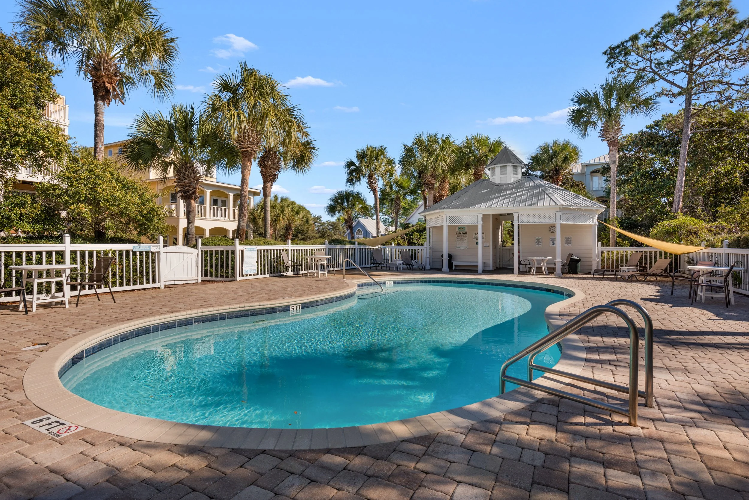 Resort-style shared pool surrounded by palm trees and lounge seating near the guest house.