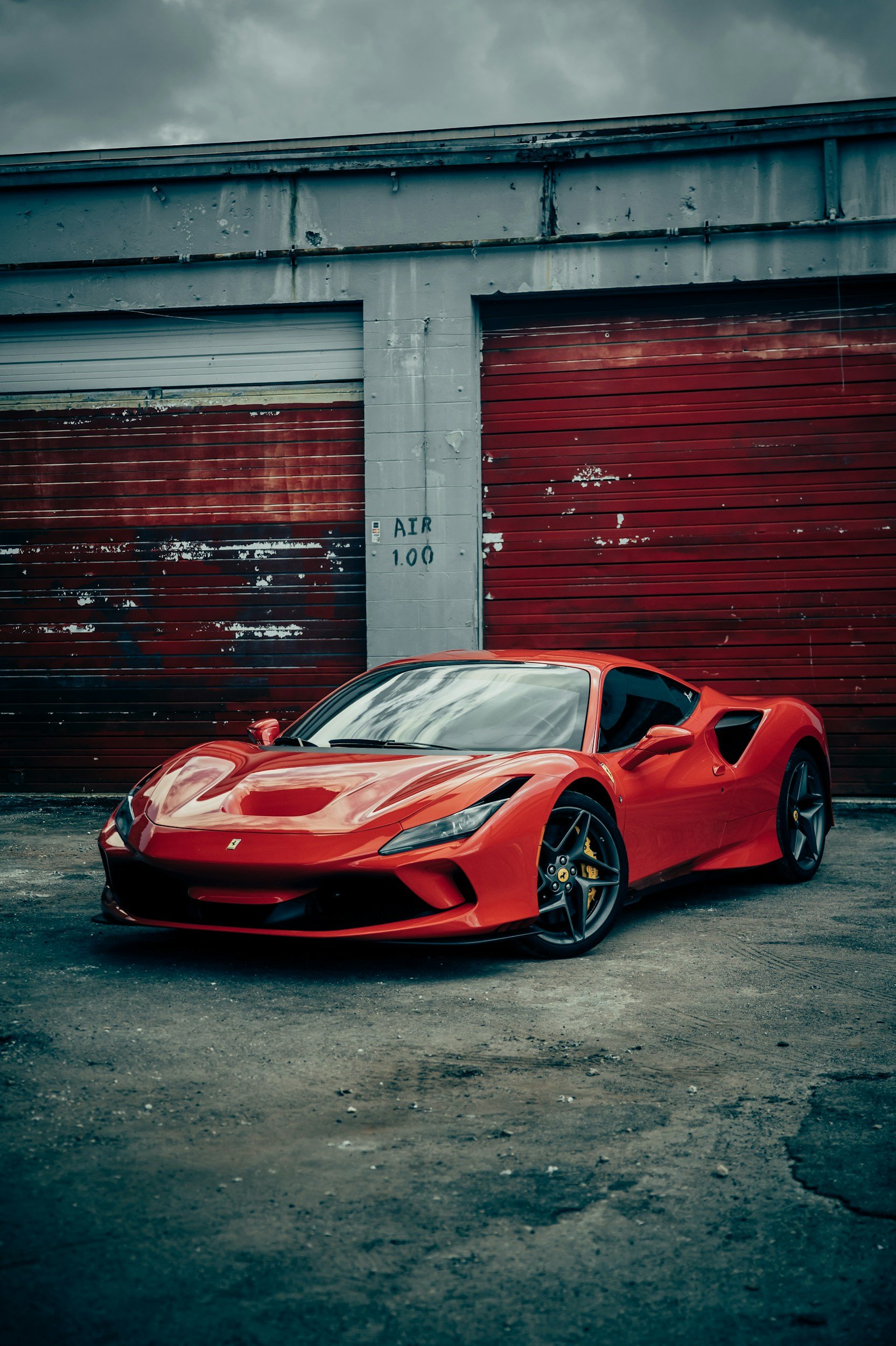 A red Ferrari sports car parked outside a building with red garage doors and a gray concrete wall.