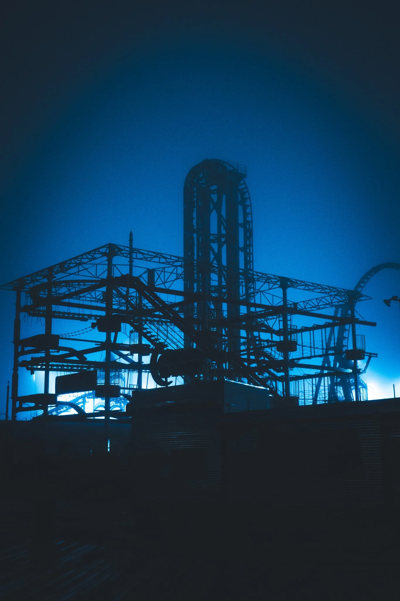 Nighttime scene of a roller coaster silhouette against a blue sky, with some clouds.