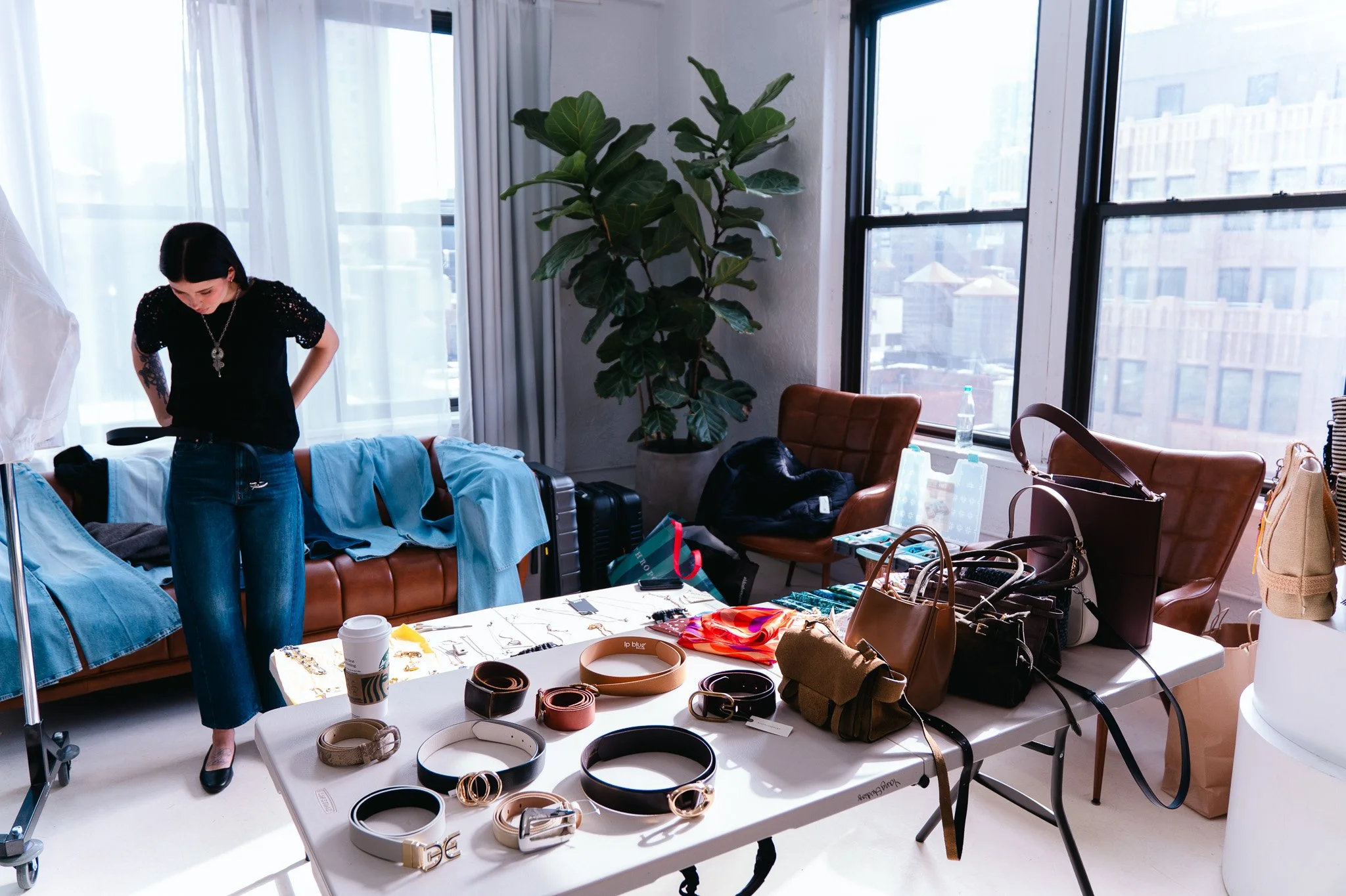 A woman standing in a bright room filled with clothing and accessories, with large windows in the background showing a cityscape.