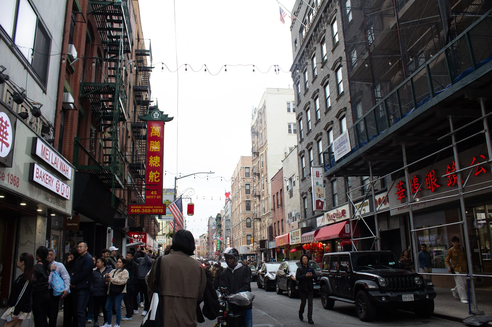 A busy city street scene with multiple pedestrians, vehicles, and storefronts, featuring Chinese signage and decorations.