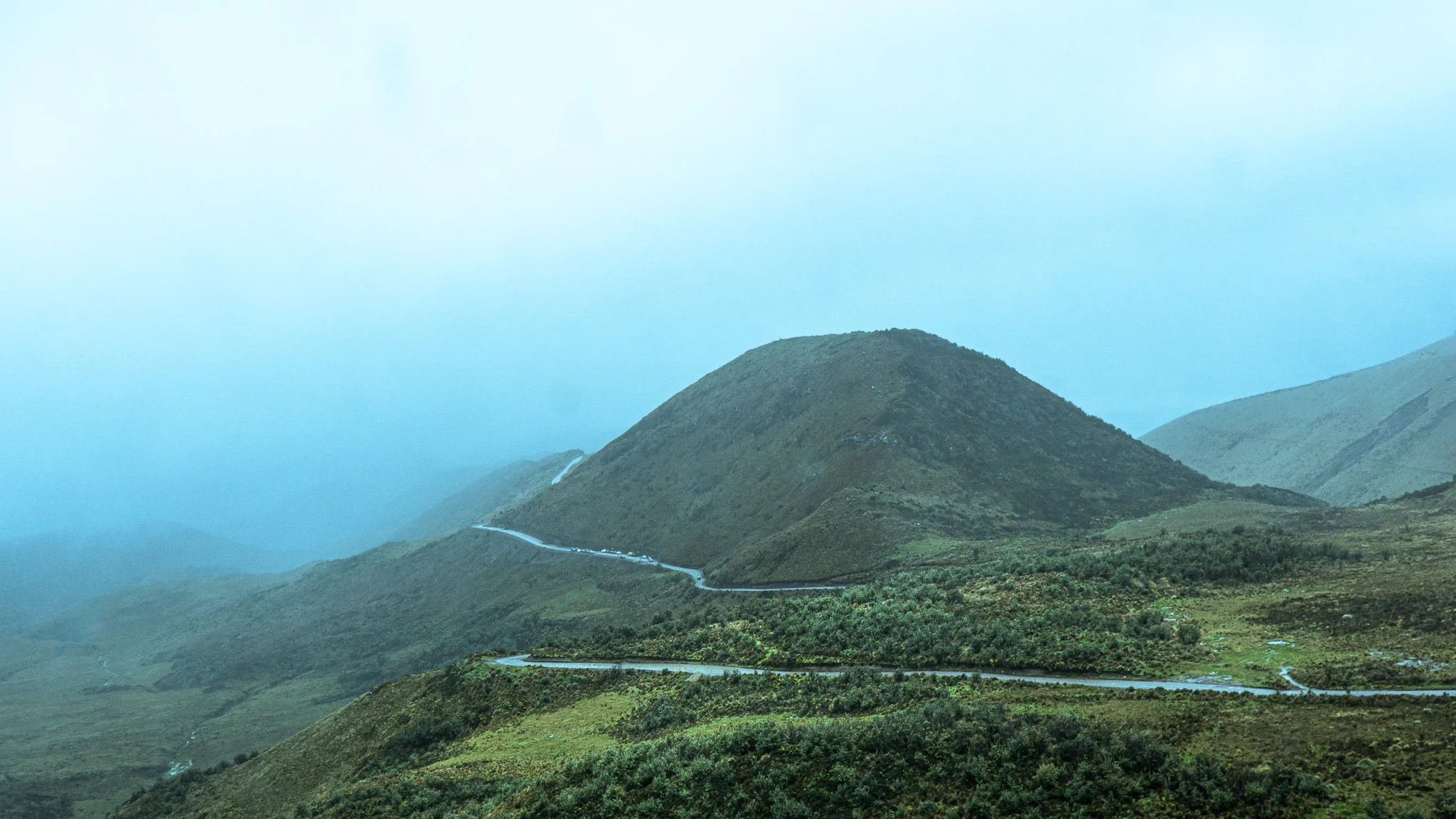 Mountains in a misty landscape with a winding road in the foreground.