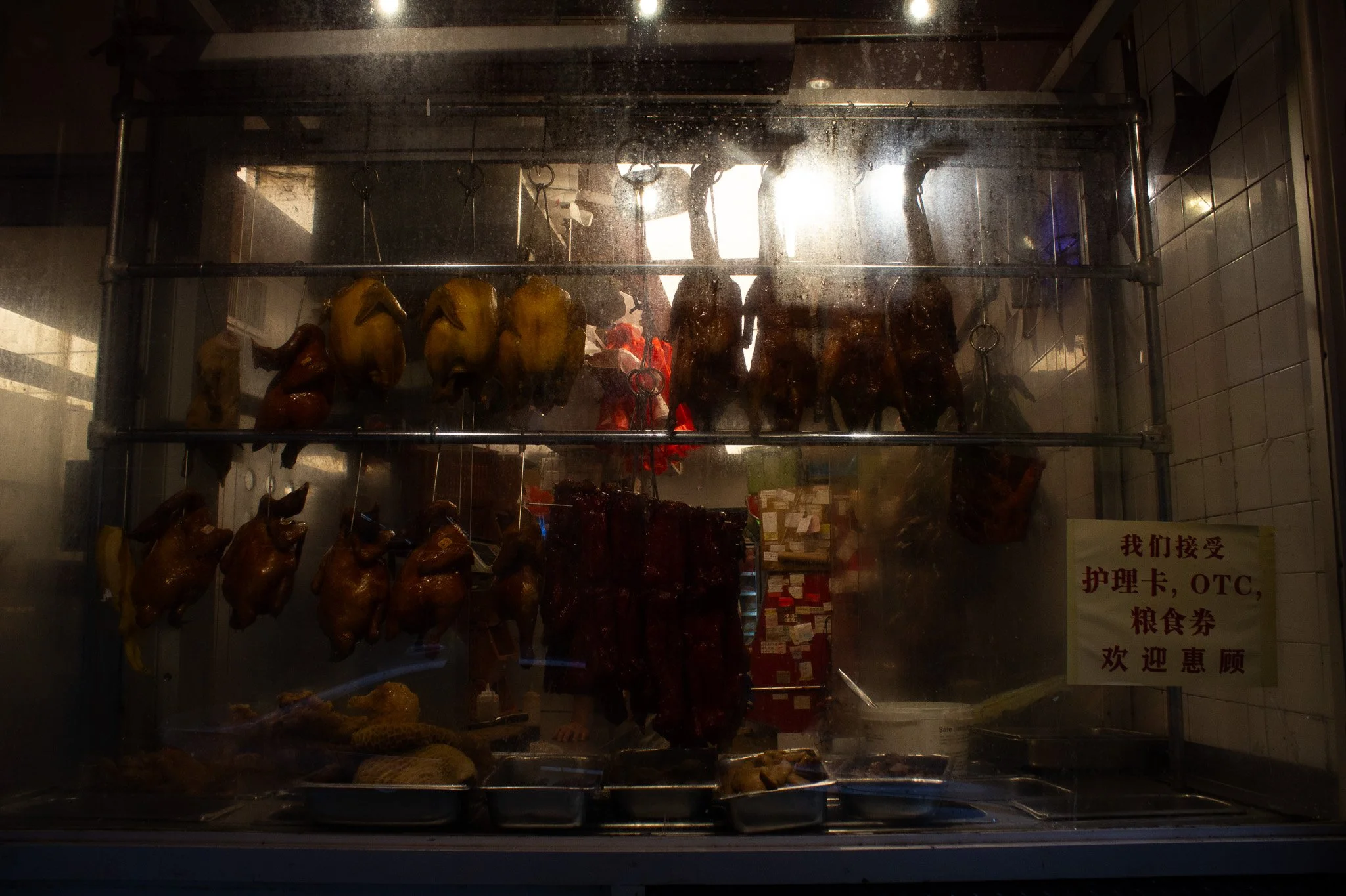 Meat and poultry displayed behind a glass case in a restaurant setting, with a sign containing Chinese characters to the right.