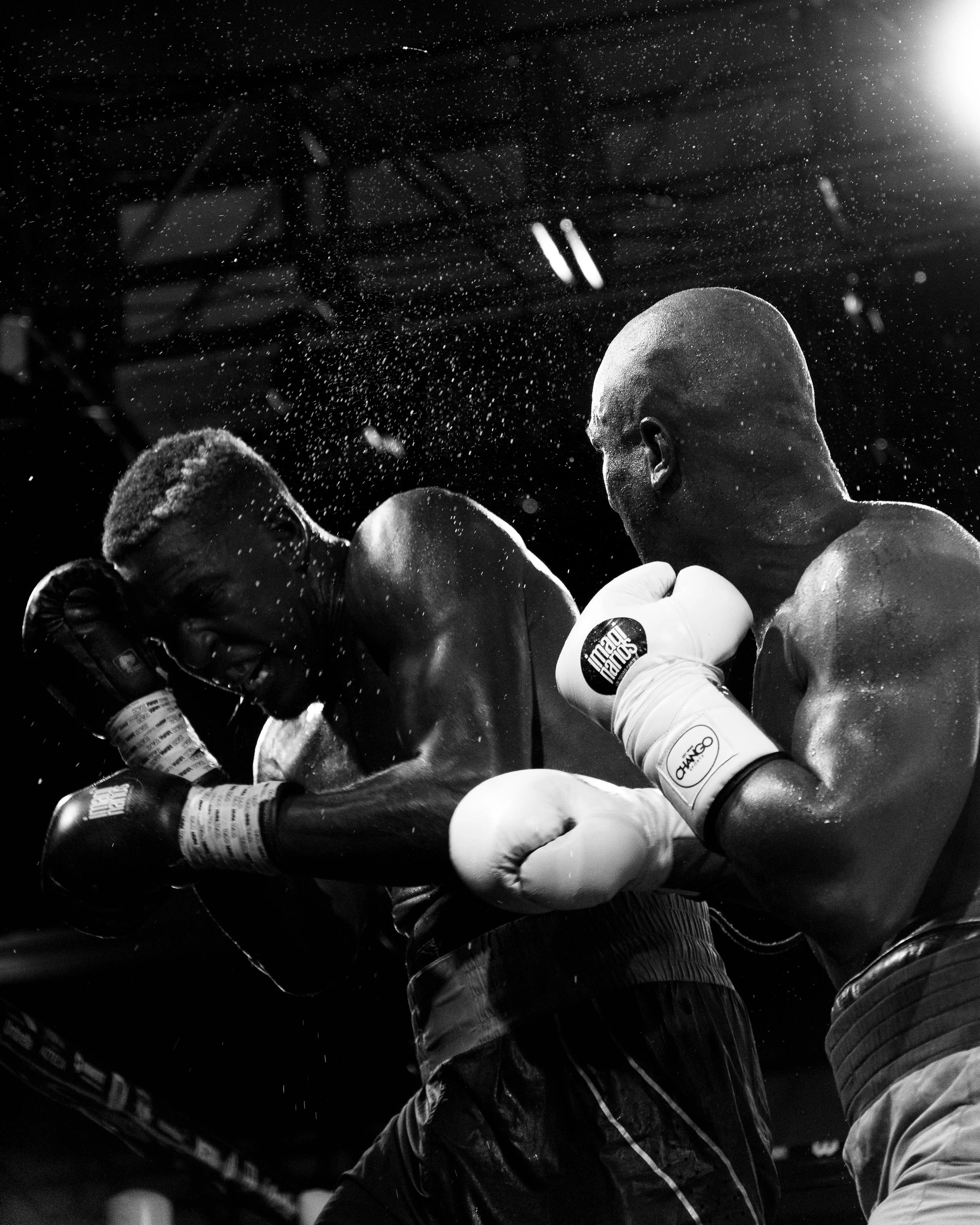 Black and white photo of two boxers in a ring, with water or sweat spray in the air, emphasizing intensity and focus.