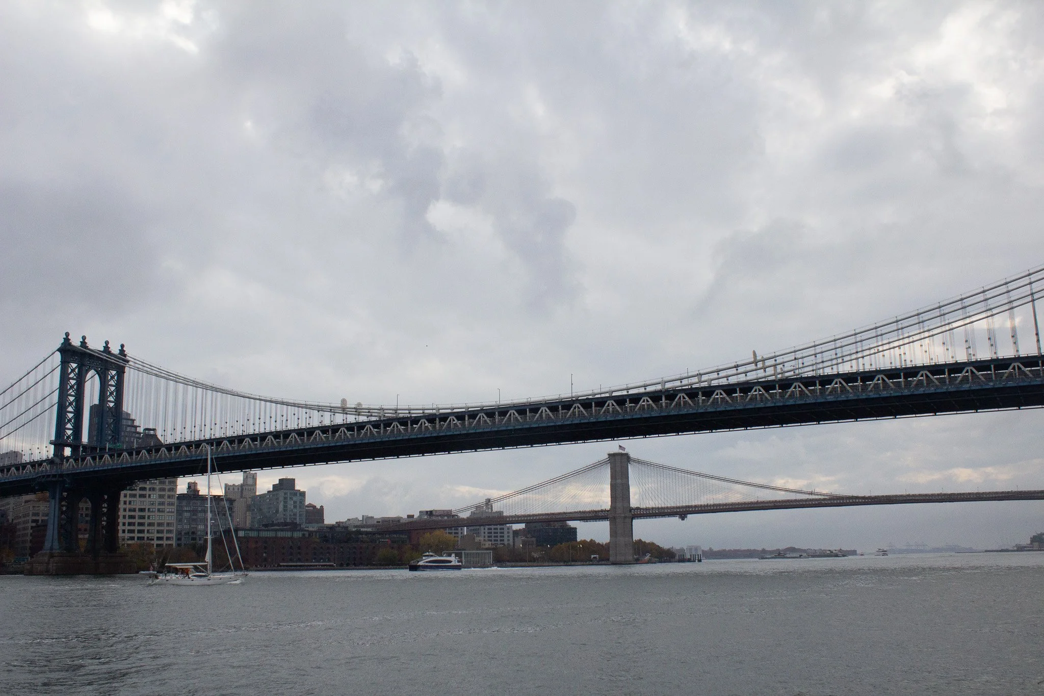 View of the Brooklyn Bridge with New York City skyline and East River under a cloudy sky.