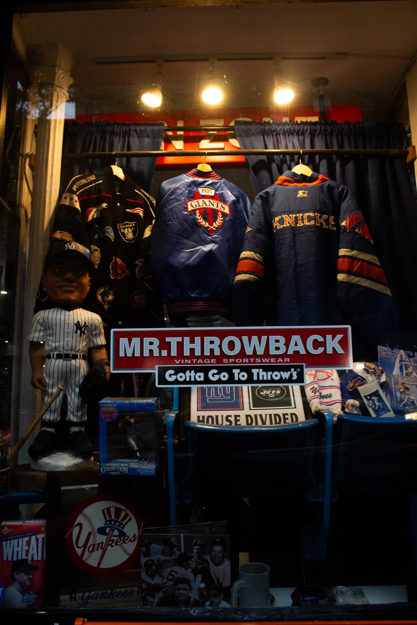 Display of vintage sportswear and memorabilia with jackets representing football teams, a bobblehead doll in a Yankees uniform, and various team memorabilia.