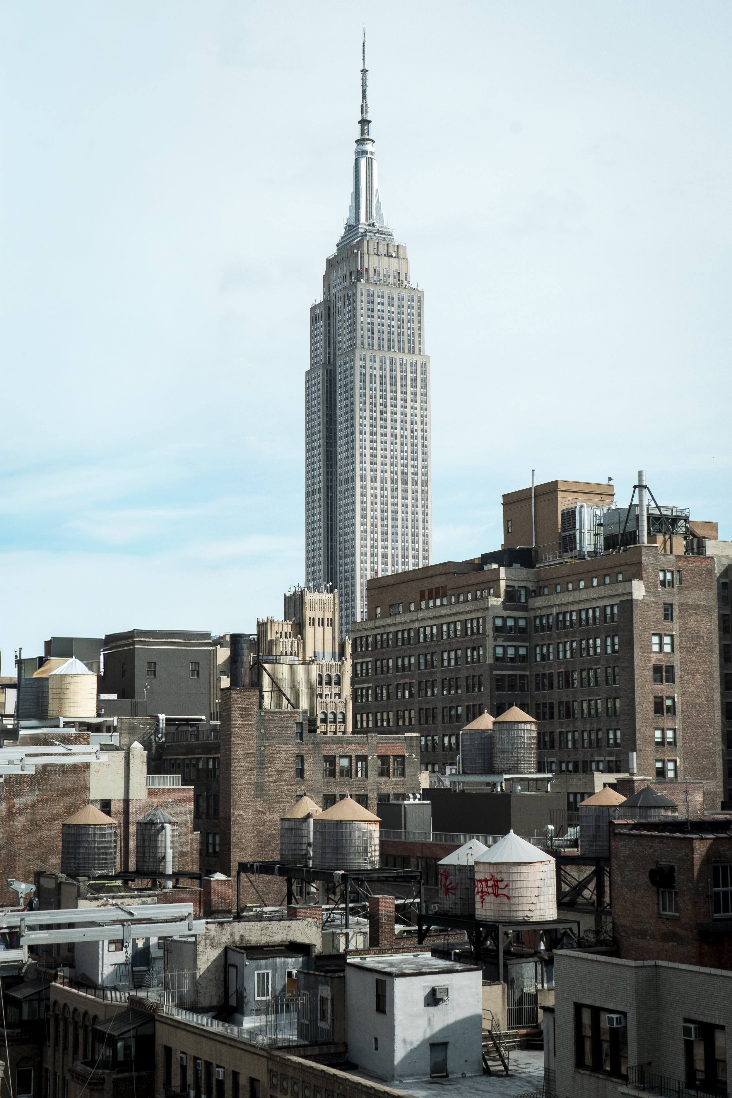 Skyline view of New York City featuring the Empire State Building, surrounded by lower-rise buildings and water towers on rooftops.