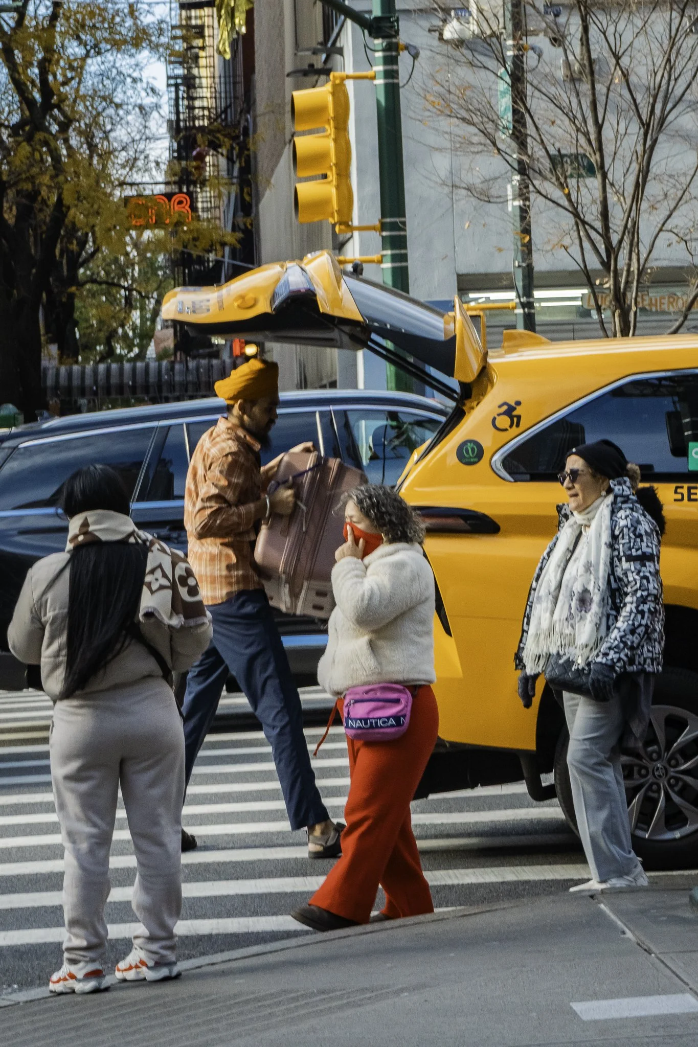 People crossing a city street at a crosswalk with yellow taxis and trees in the background during daytime.