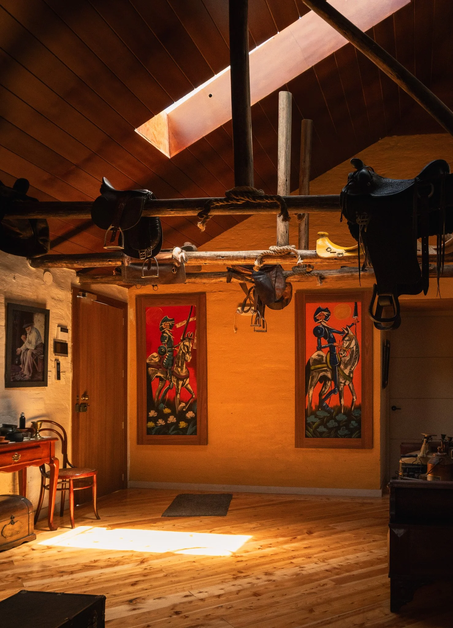 Interior of a room with wooden floor and walls, featuring riding-themed artwork on the walls, and a wooden bar or counter on the left side.