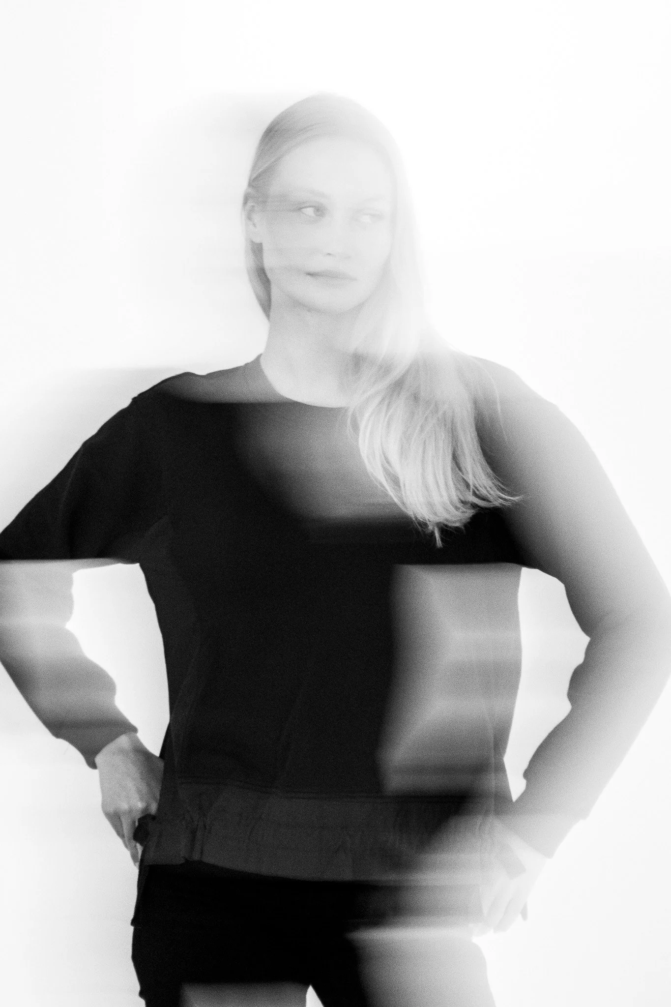 A woman with long hair wearing a dark top posing with her hands on her hips against a plain background.
