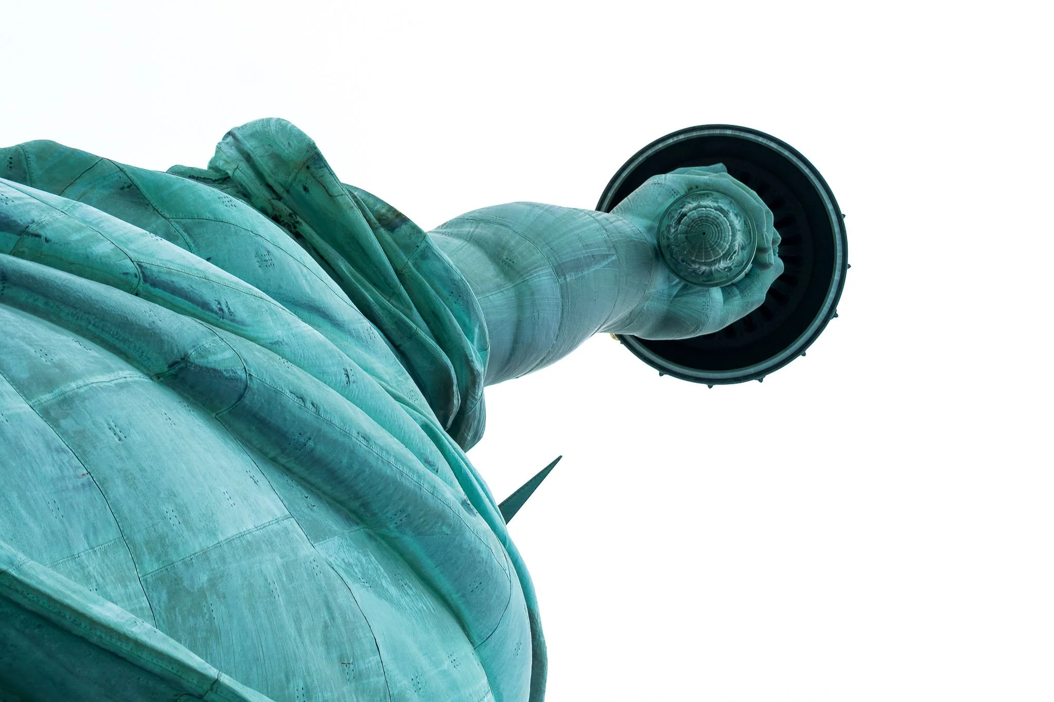 Close-up of the base and tower of the Statue of Liberty against a white sky background.