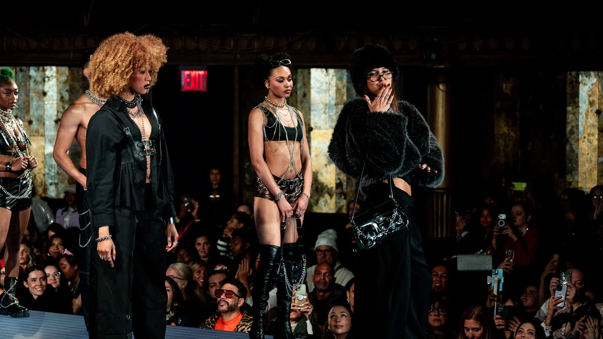Models walking down runway during fashion show, audience watching and taking photos