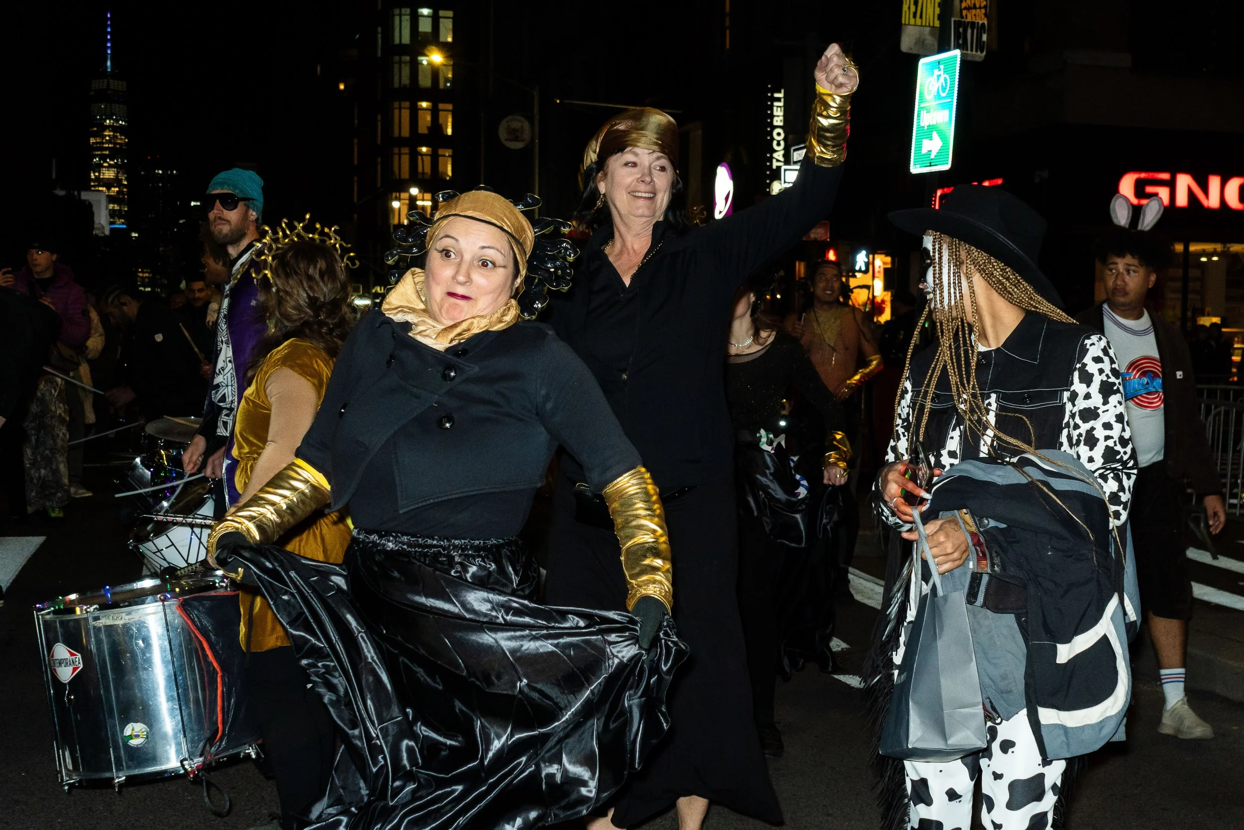 People celebrating at night in a city street, wearing costumes with gold and animal print details.