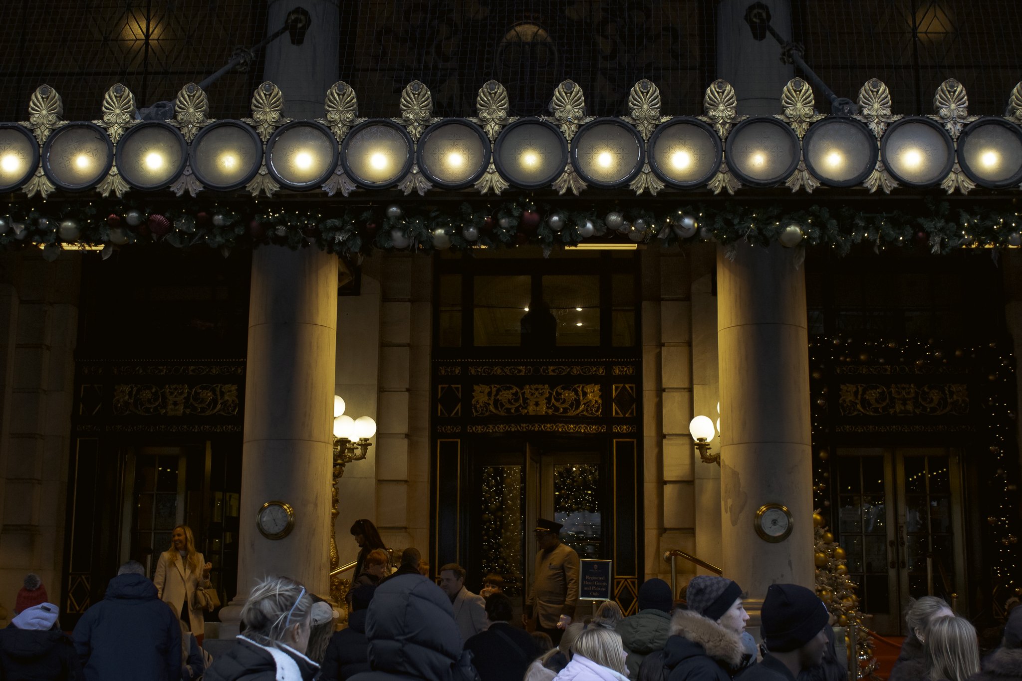 People gathered inside a decorated building with gold accents, an illuminated sign, and Christmas decorations, likely during a holiday event.