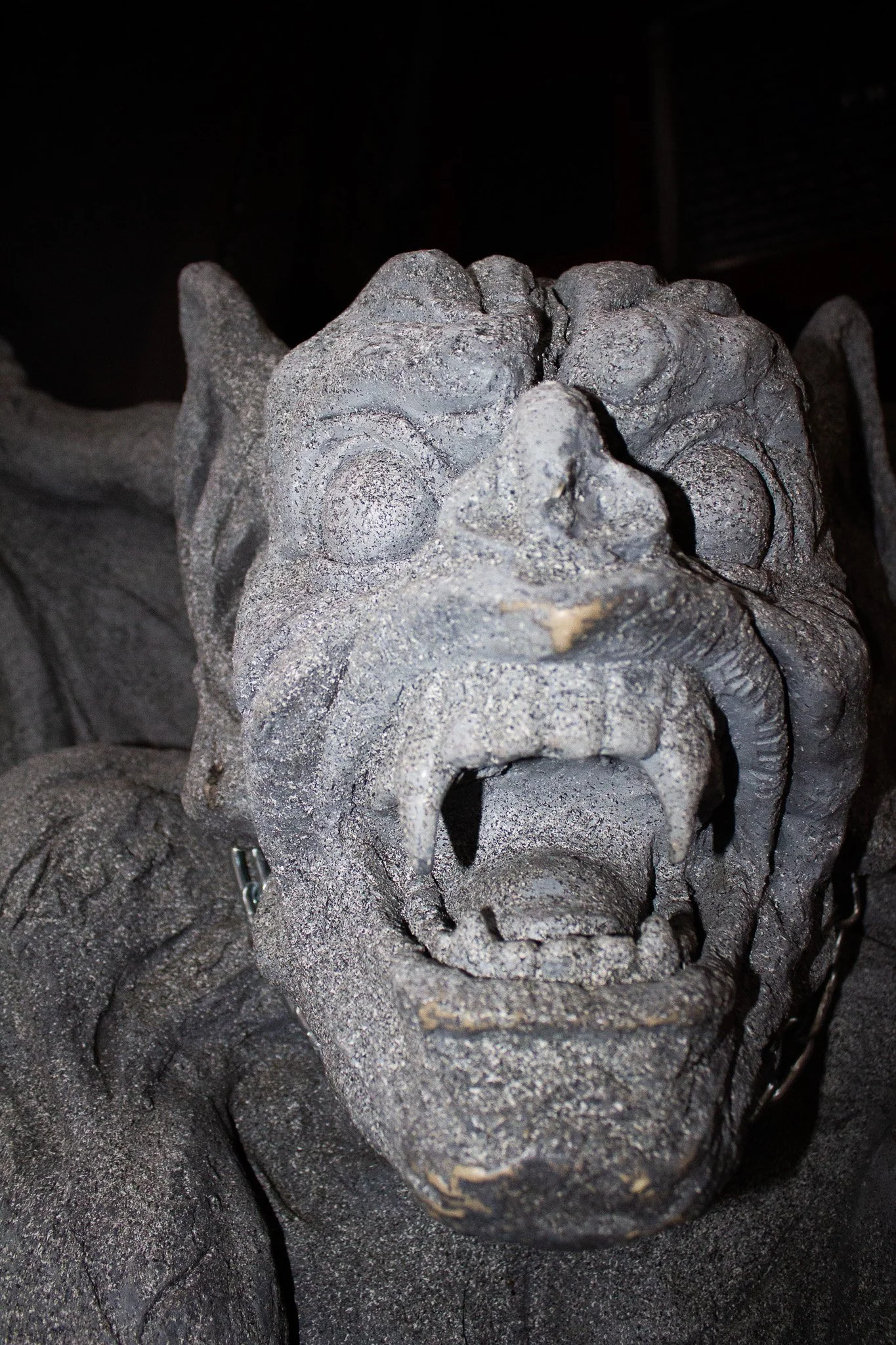 Close-up of an ancient stone sculpture of a fierce face, possibly a mythical creature or deity, with an open mouth showing teeth and detailed facial features.