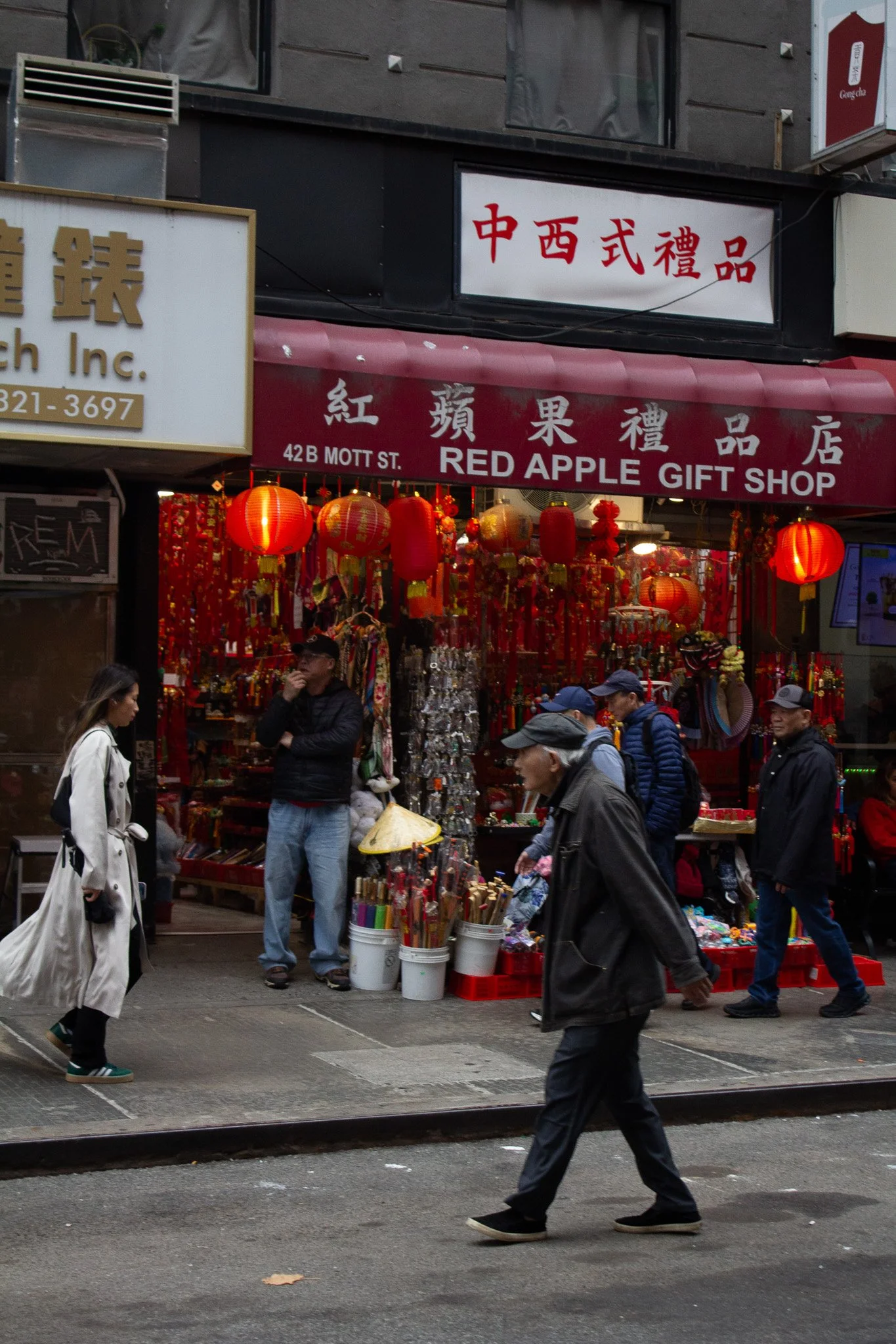 Street scene in front of an Asian gift shop decorated with red lanterns and decorations, with several pedestrians walking by.