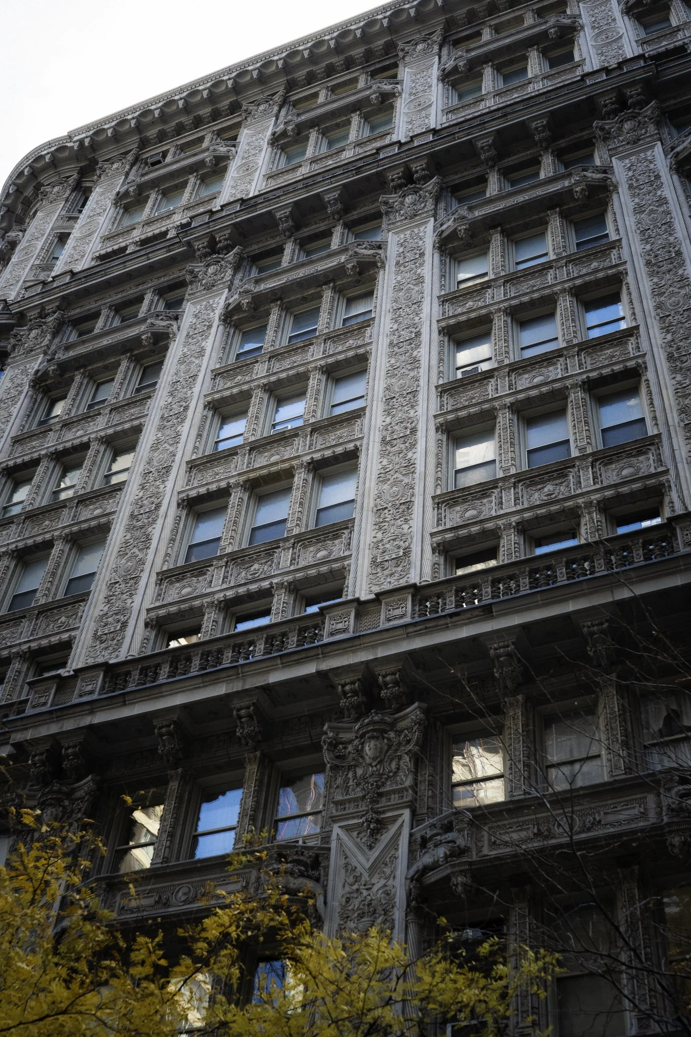 Ornate historic building with decorative stonework and intricate details, partially obscured by yellow-leafed trees.