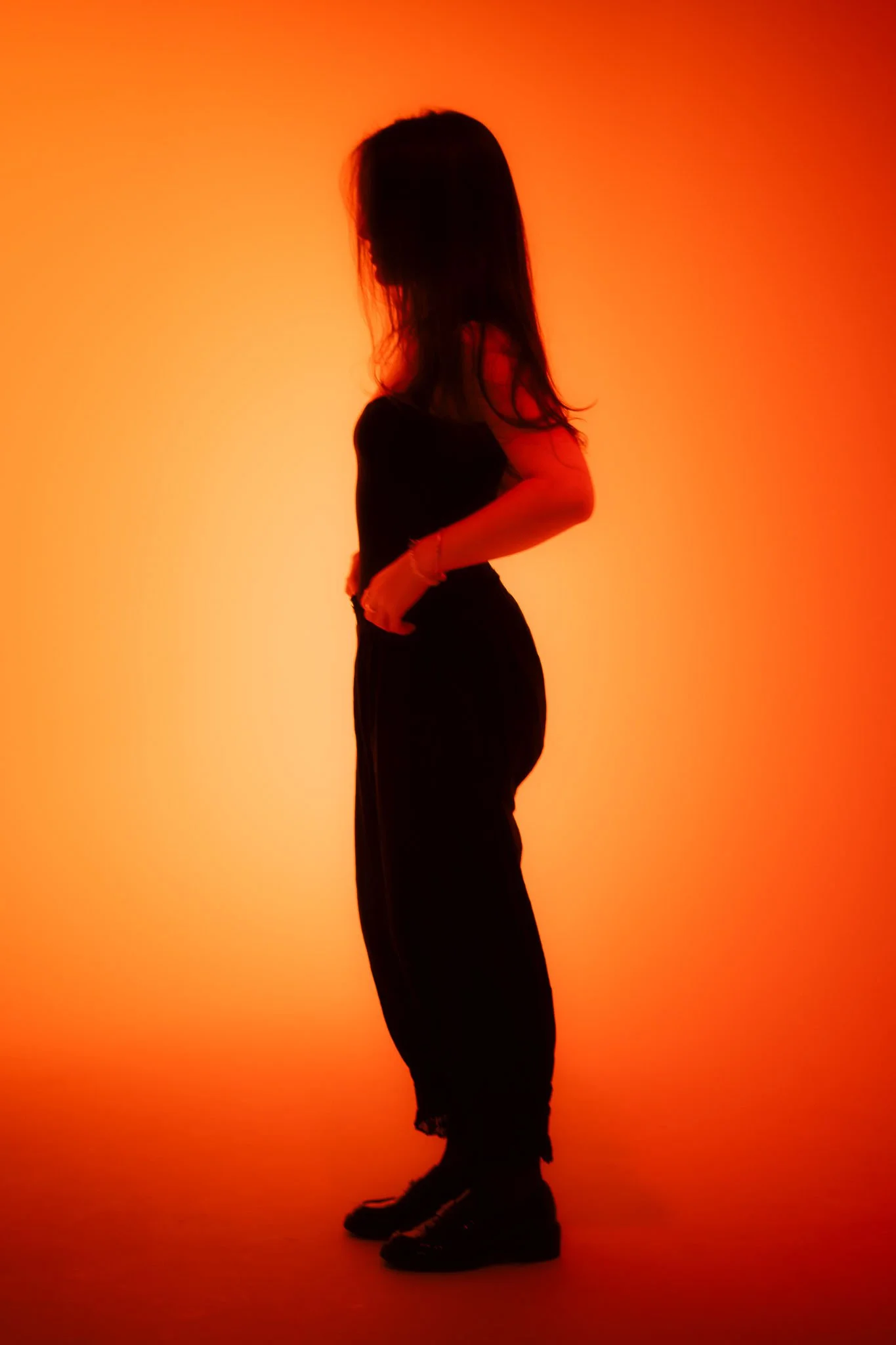 Silhouette of a woman in a black outfit standing against a warm orange background.