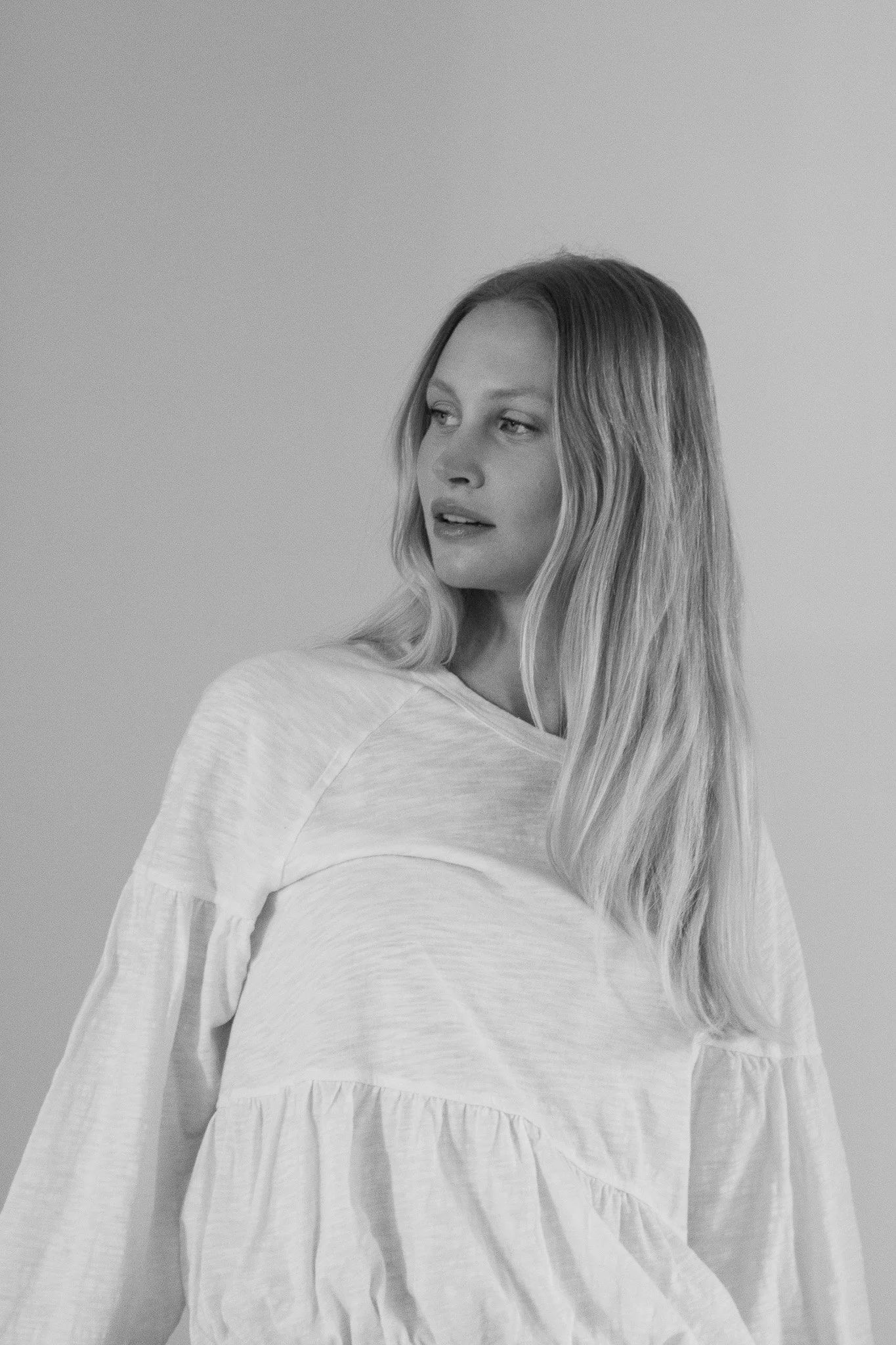 Black and white photo of a woman with long blonde hair wearing a light-colored, loose blouse, looking to her left.