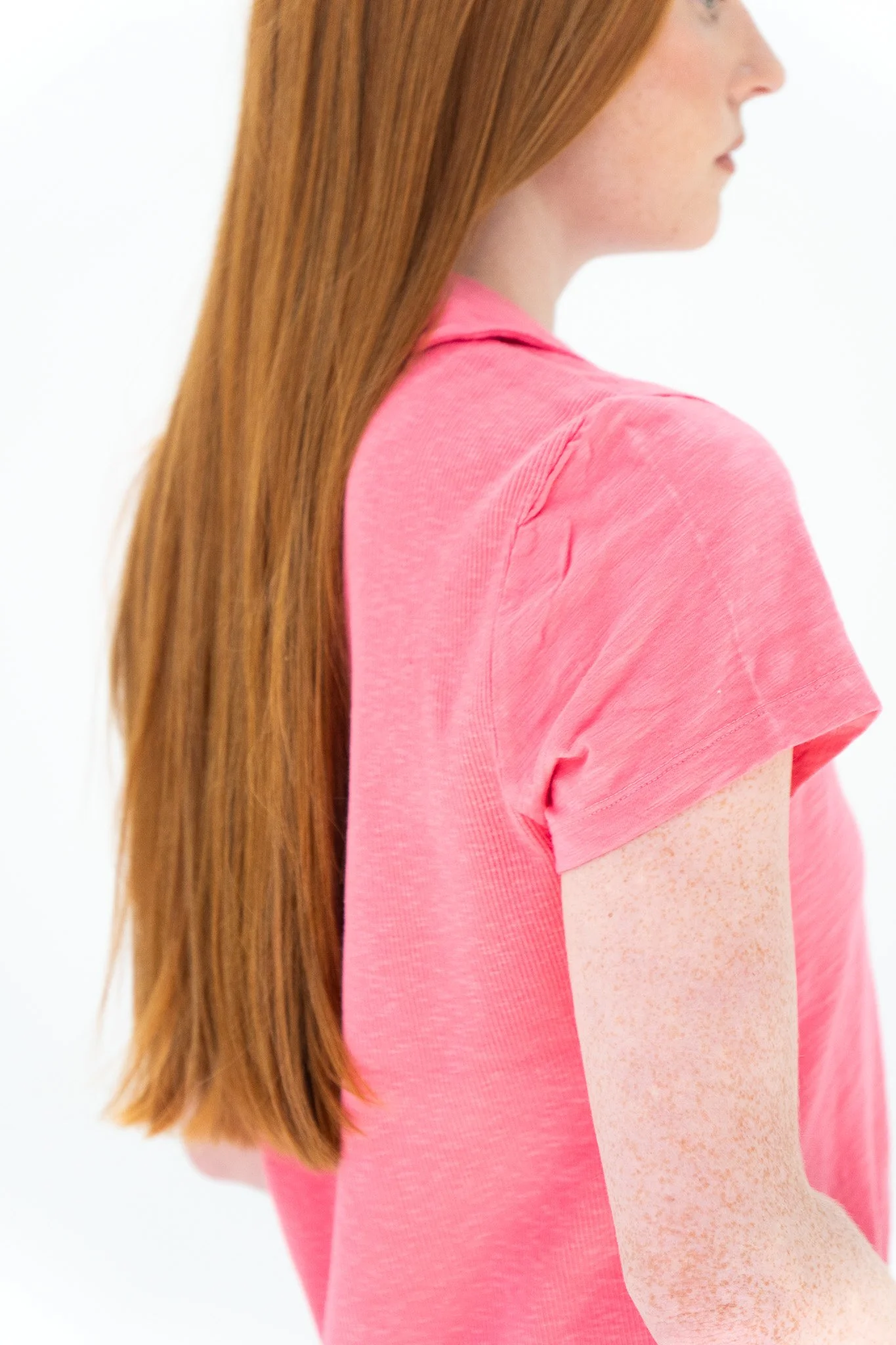 Side view of a person with long red hair wearing a pink shirt against a white background.