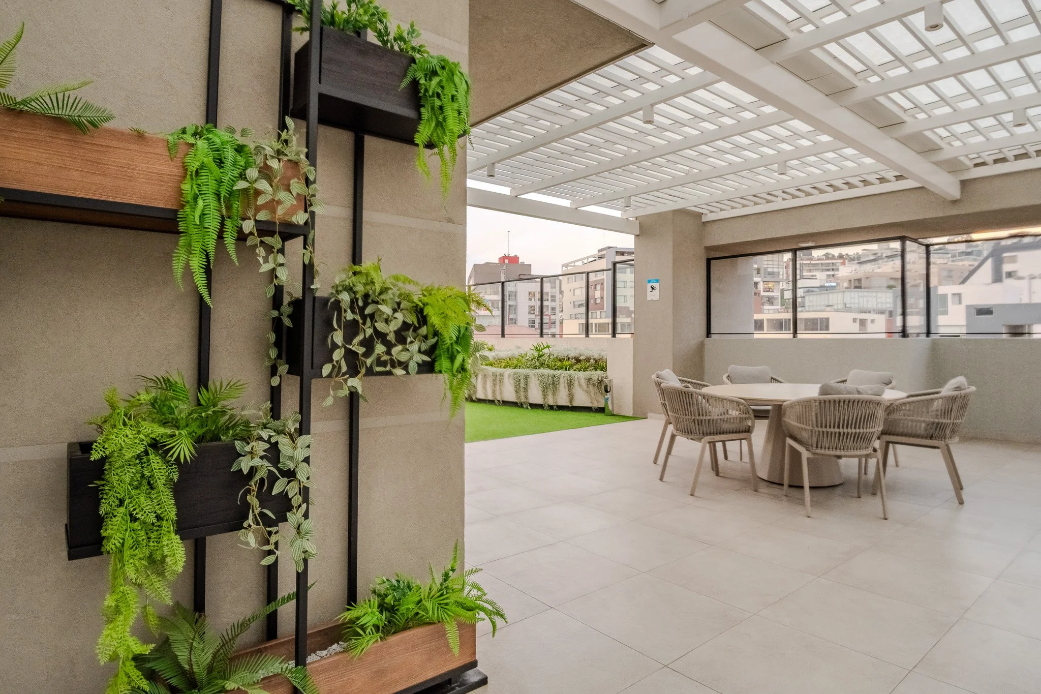 Balcony with potted plants on shelves, outdoor seating with cushioned chairs, city buildings in the background, and a glass railing.