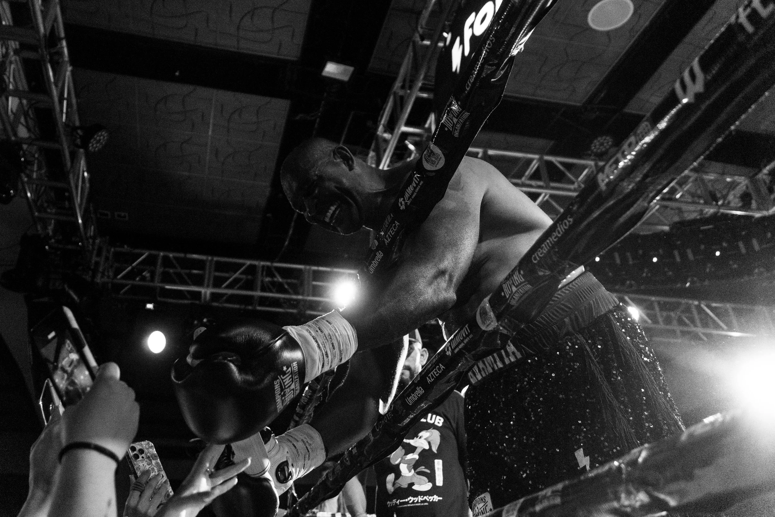A boxer with gloves and shorts in a boxing ring, celebrating a victory with a trophy, under bright lights with a dark background.