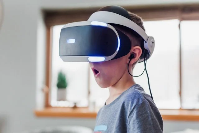 A young boy wearing a virtual reality headset with a surprised expression in a bright room.