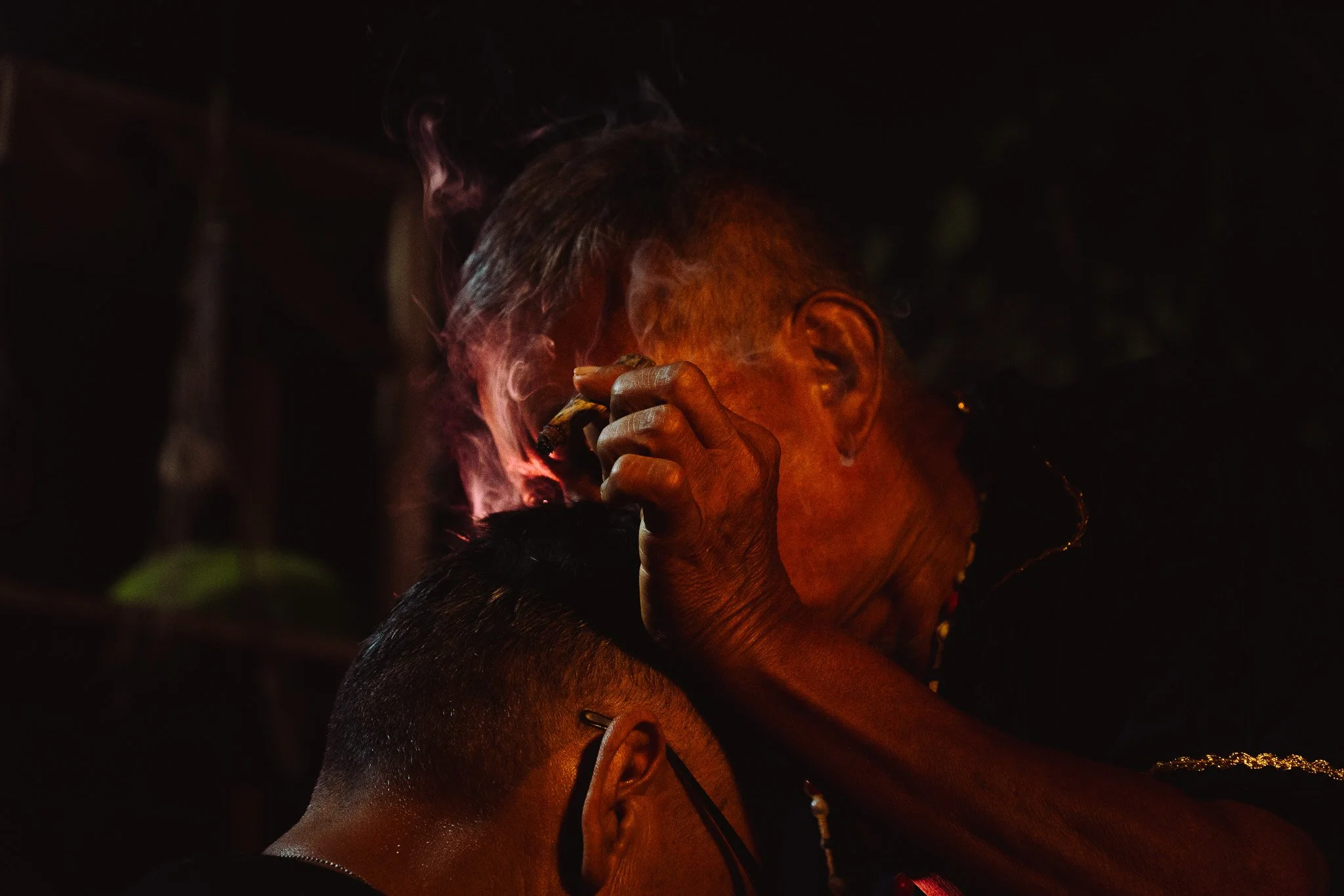 Two women, one with short gray hair and the other with dark hair, smoking at night, illuminated by a warm light.