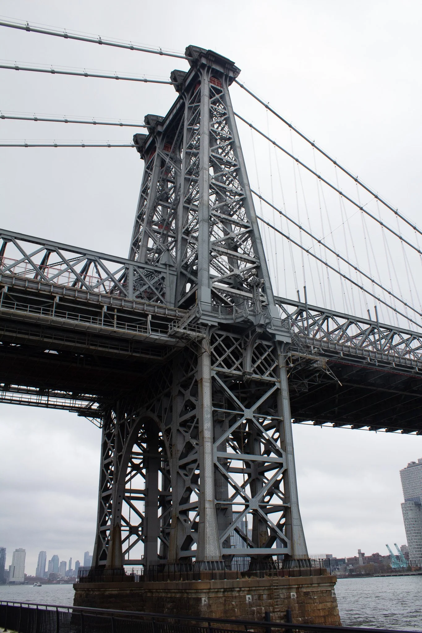 A steel suspension bridge with a tall, intricate tower and cables extending from it, over a river.