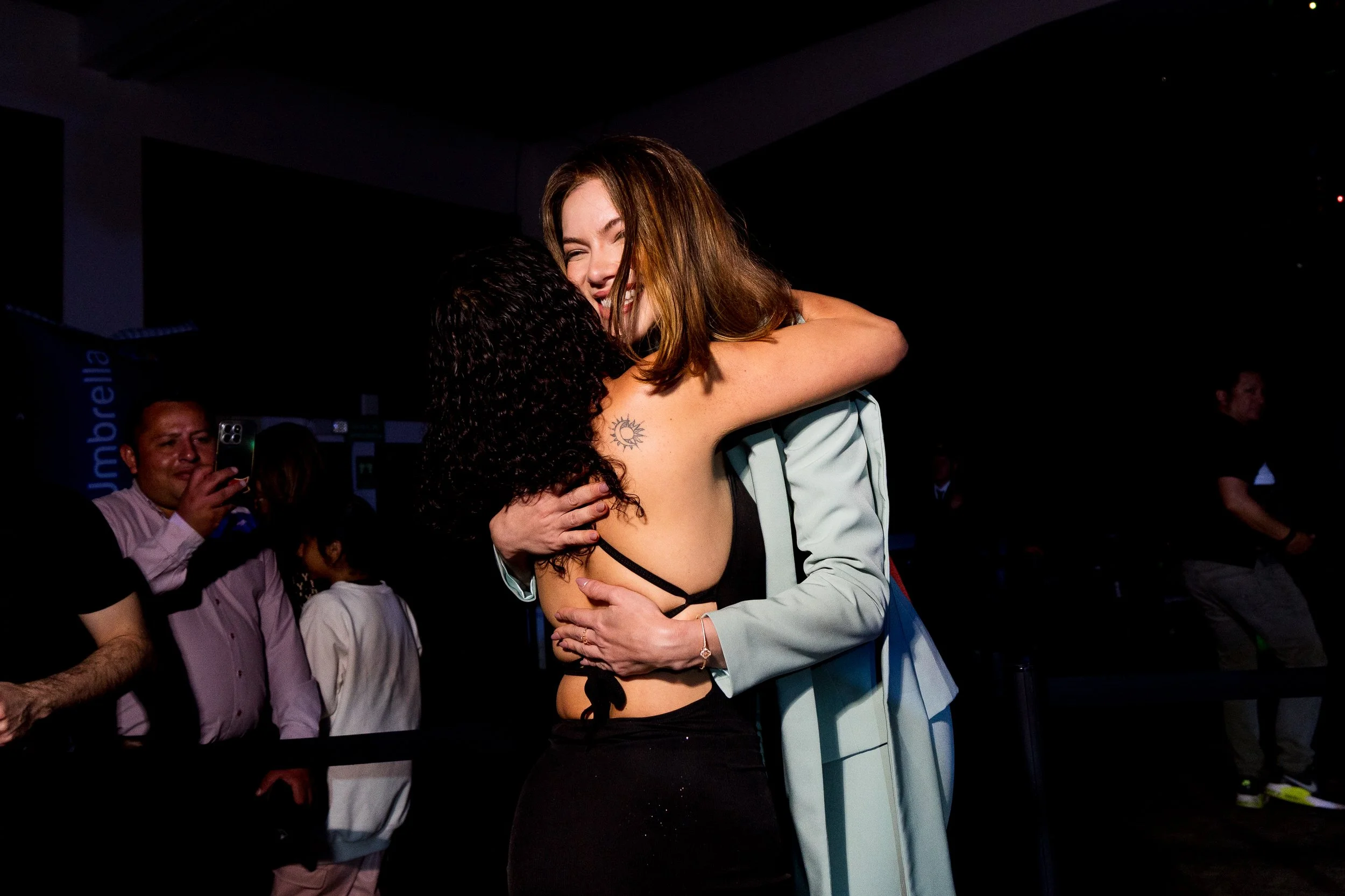 Two women hugging at an indoor event, smiling and embracing each other warmly.