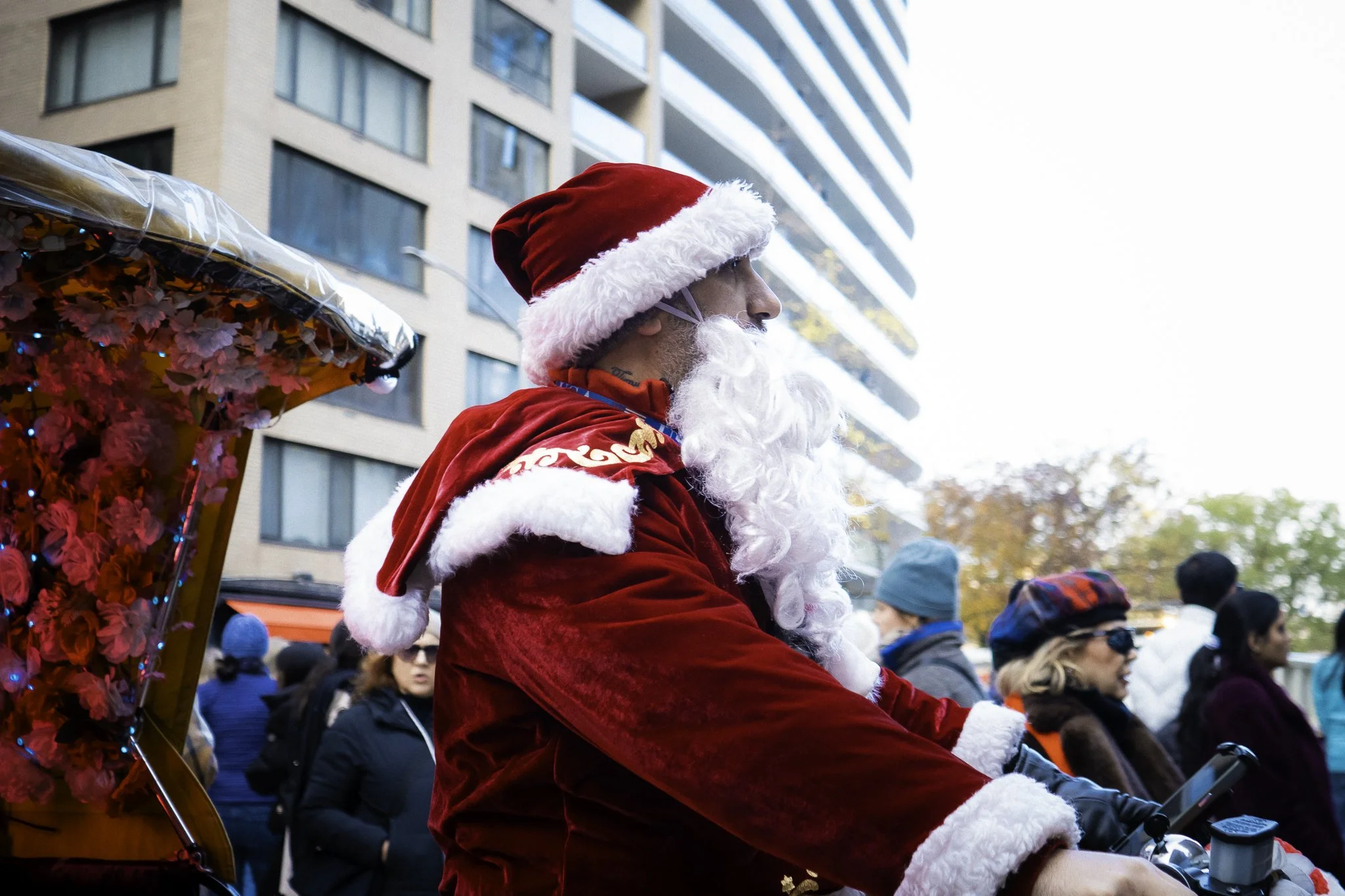 A man dressed as Santa Claus riding a motorcycle during a parade with a crowd of people watching.