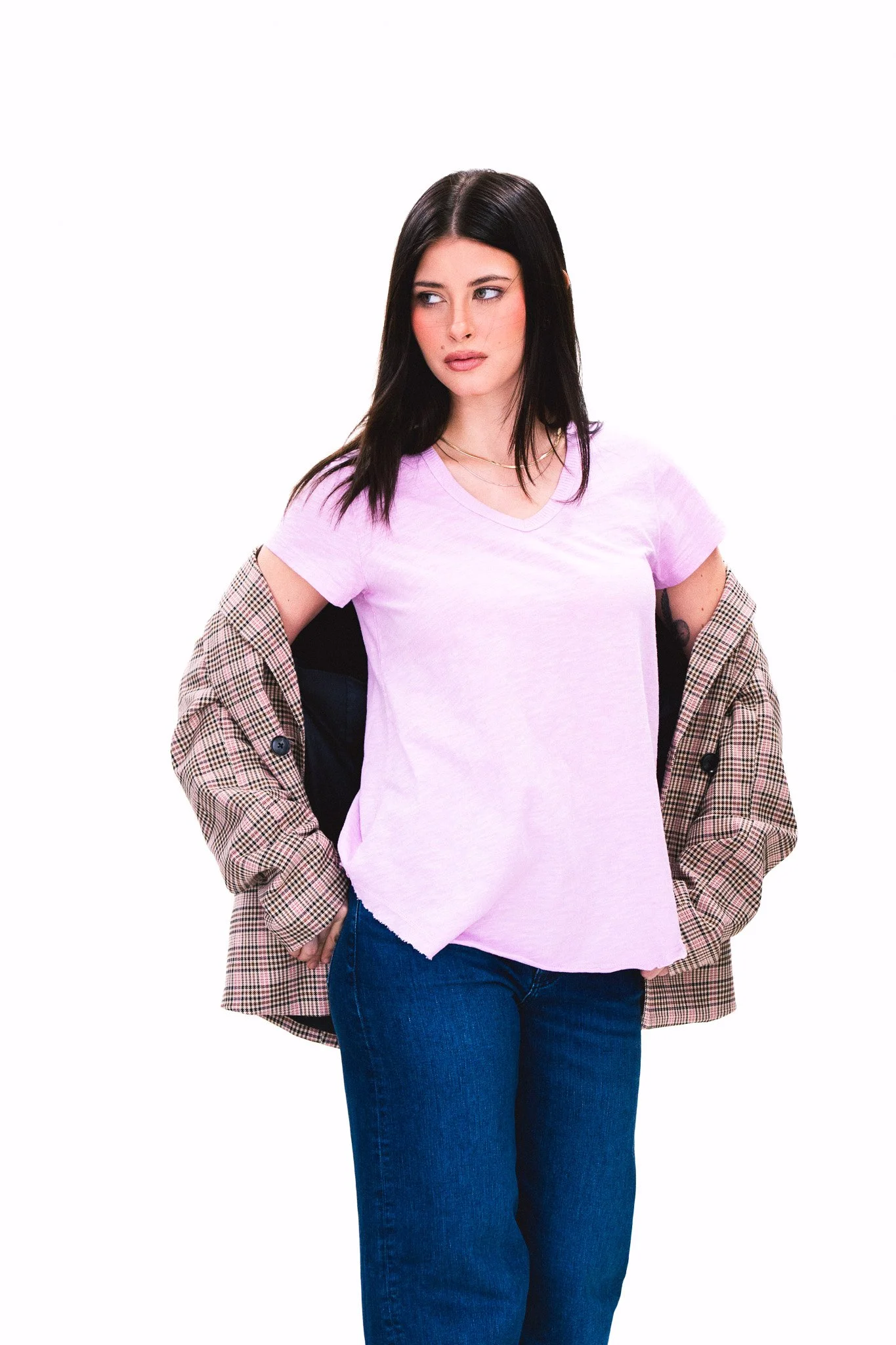 A woman with straight dark hair wearing a light purple T-shirt, a checkered jacket hanging off her shoulders, and blue jeans.