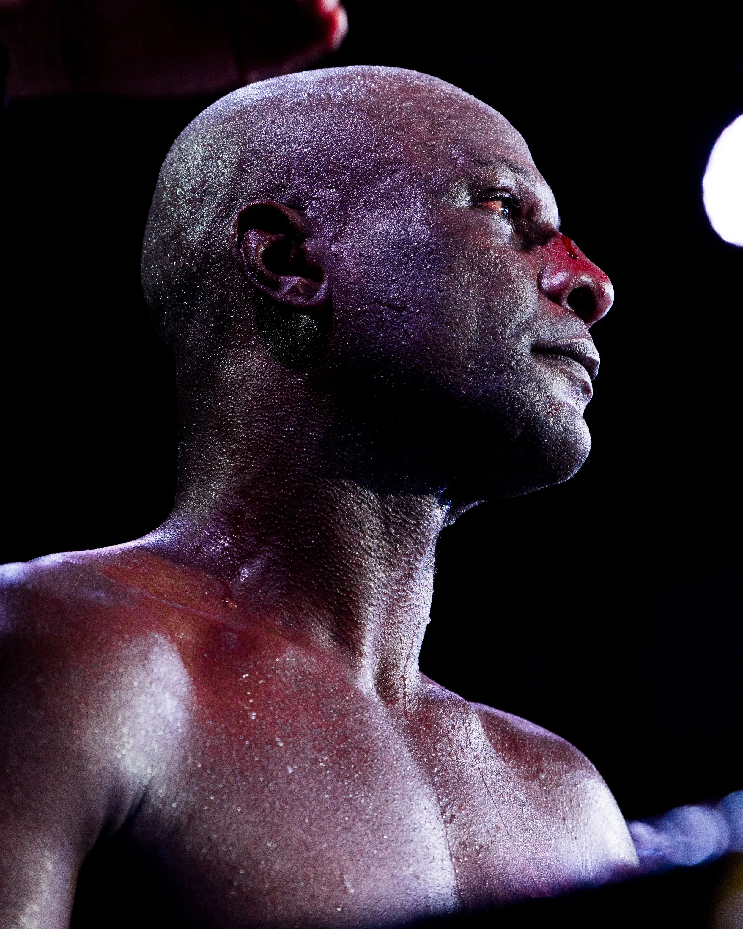 Close-up of a person with glitter on their face and body, looking to the side against a dark background.