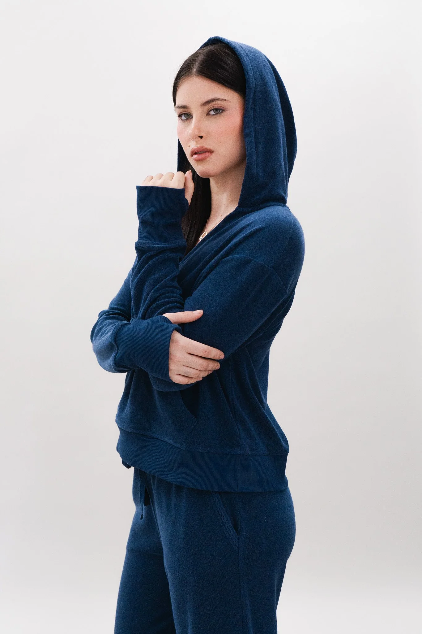 A young woman with dark hair wearing a navy blue hoodie and matching pants standing against a plain white background.