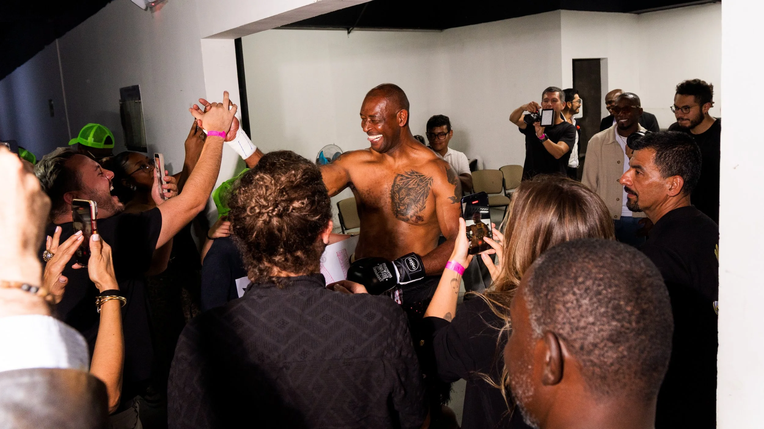 A shirtless man with tattoos smiling and high-fiving people in a crowded indoor setting.