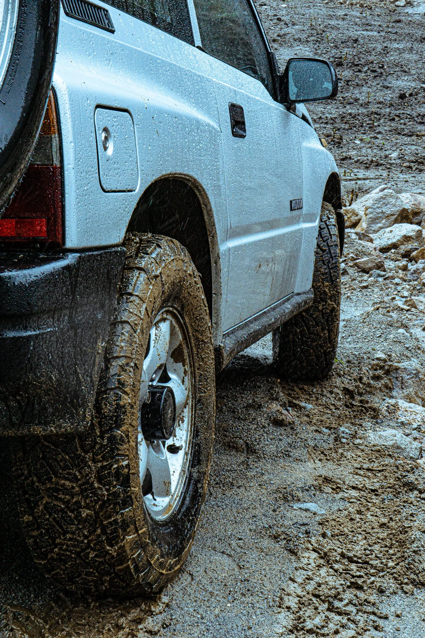 A white SUV with muddy tires parked on a wet, muddy ground during rain.