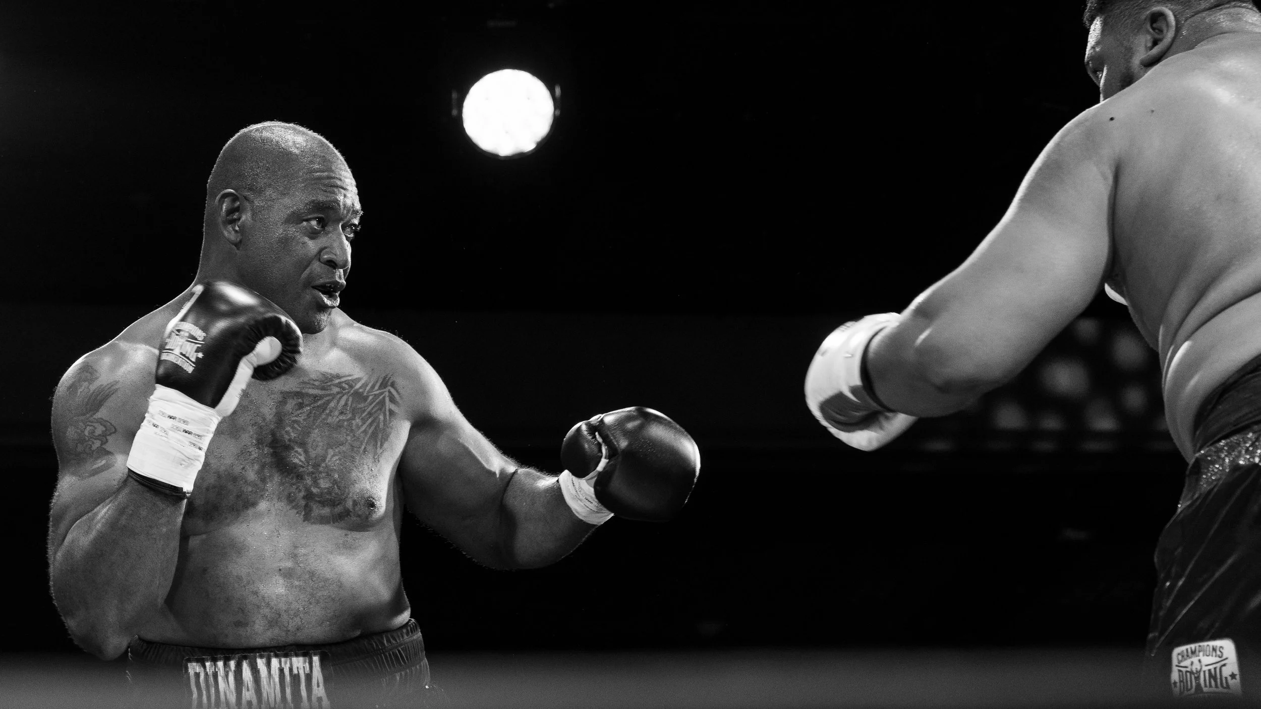Black and white photograph of two male boxers in a match, one delivering a punch to the other's face.