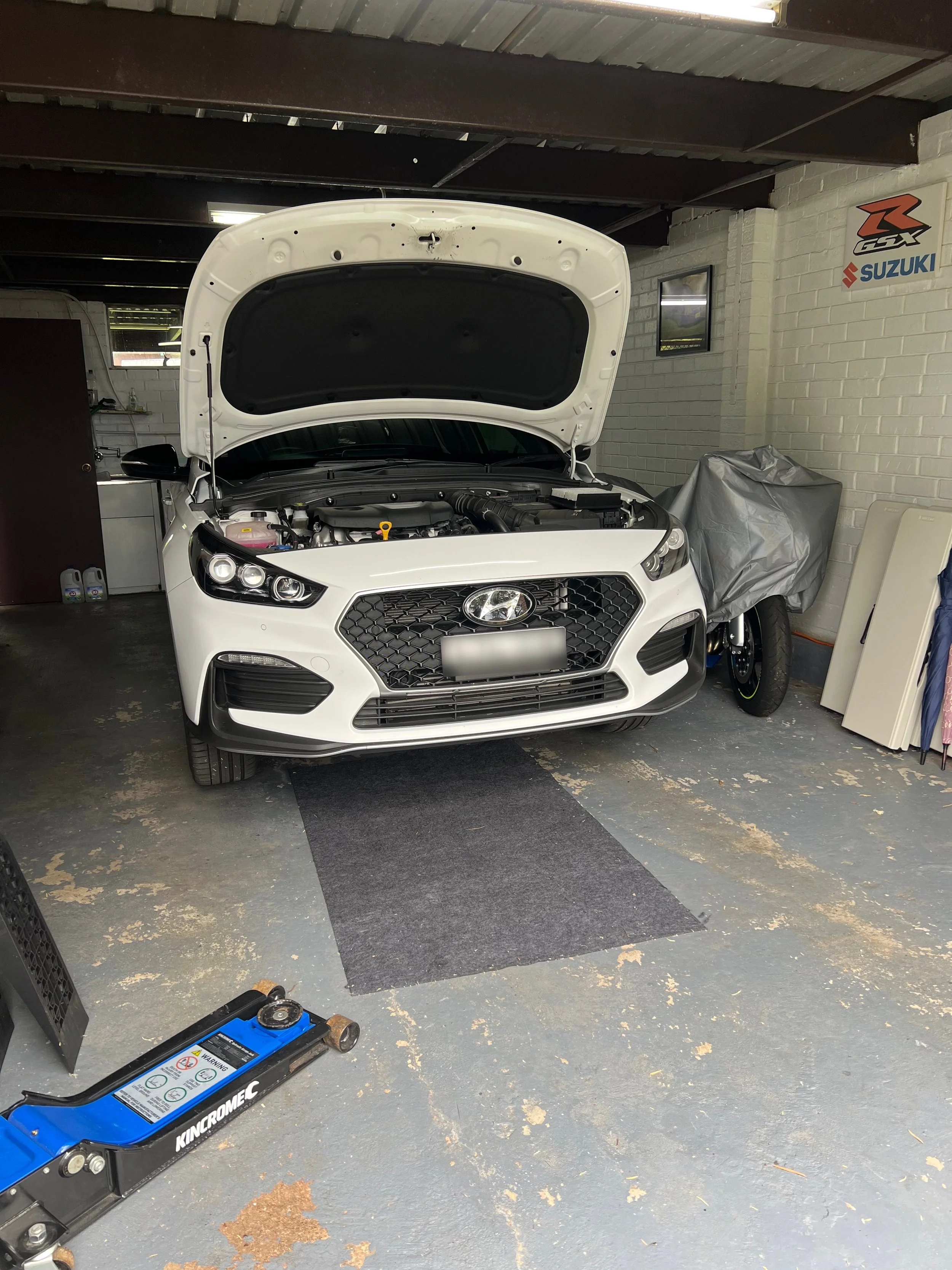 A white Hyundai car with its hood open inside a garage, with tools and equipment around.