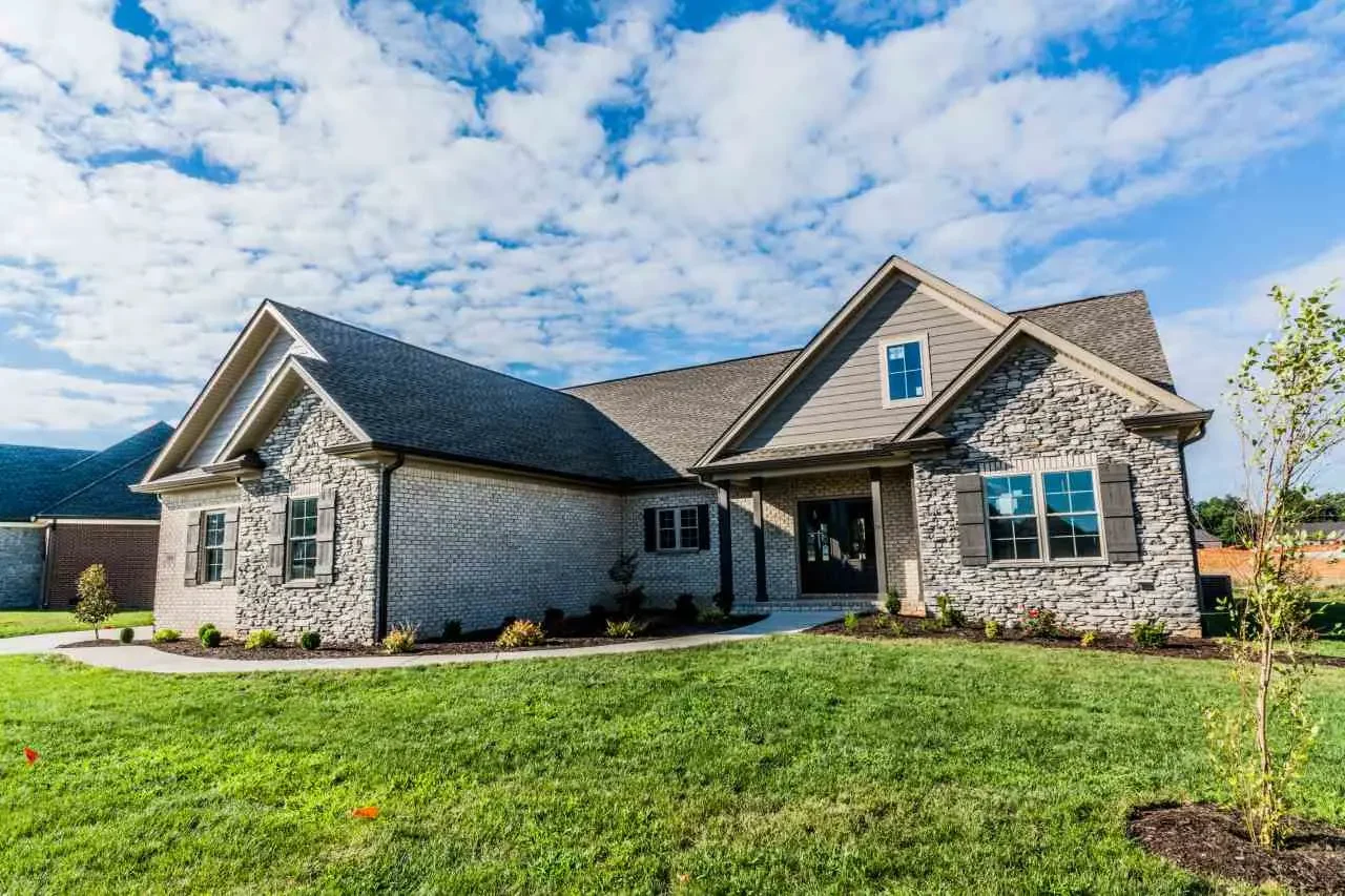 A large modern house with stone and siding exterior, multiple gables, and a well-maintained front yard with grass and small plants.
