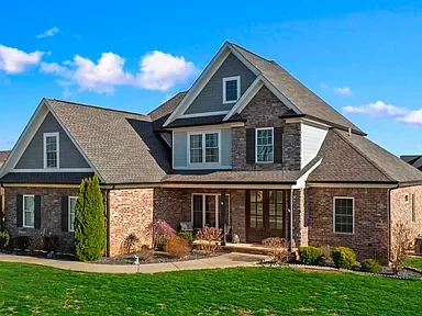 A modern two-story house with brick and siding exterior, a well-maintained lawn, and a clear blue sky.