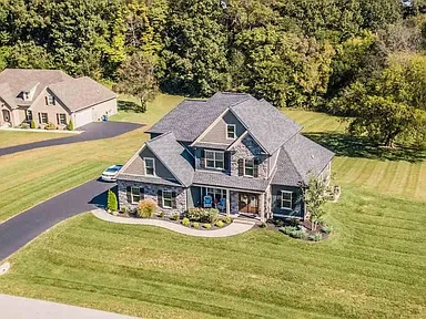 A large, two-story suburban house with a gray roof, surrounded by a well-maintained lawn and trees. Roofing size and types of roofs matter. Consult our professional team.