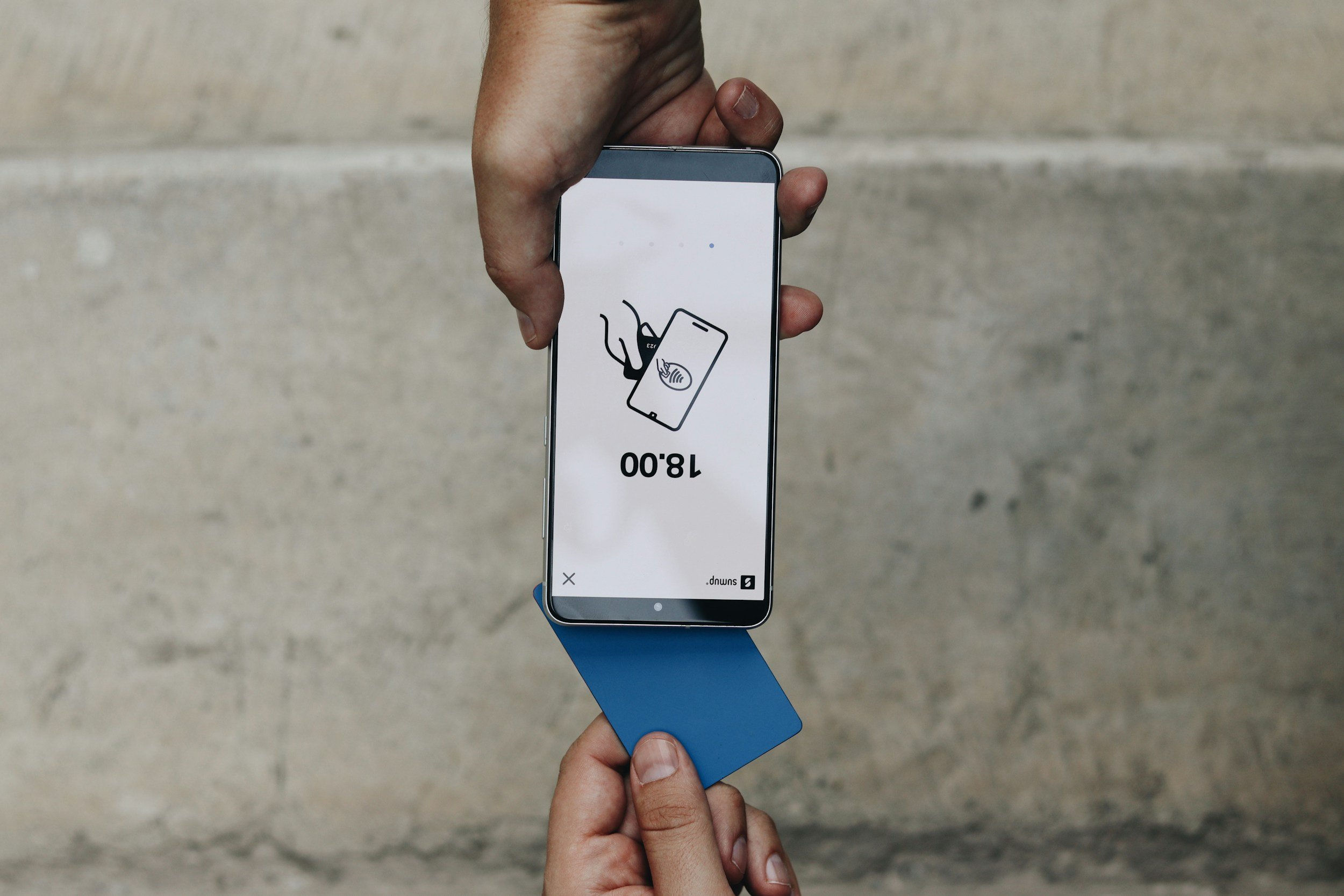 Person holding a smartphone and a card, with the phone displaying a digital access or identification scan, against a concrete wall background.