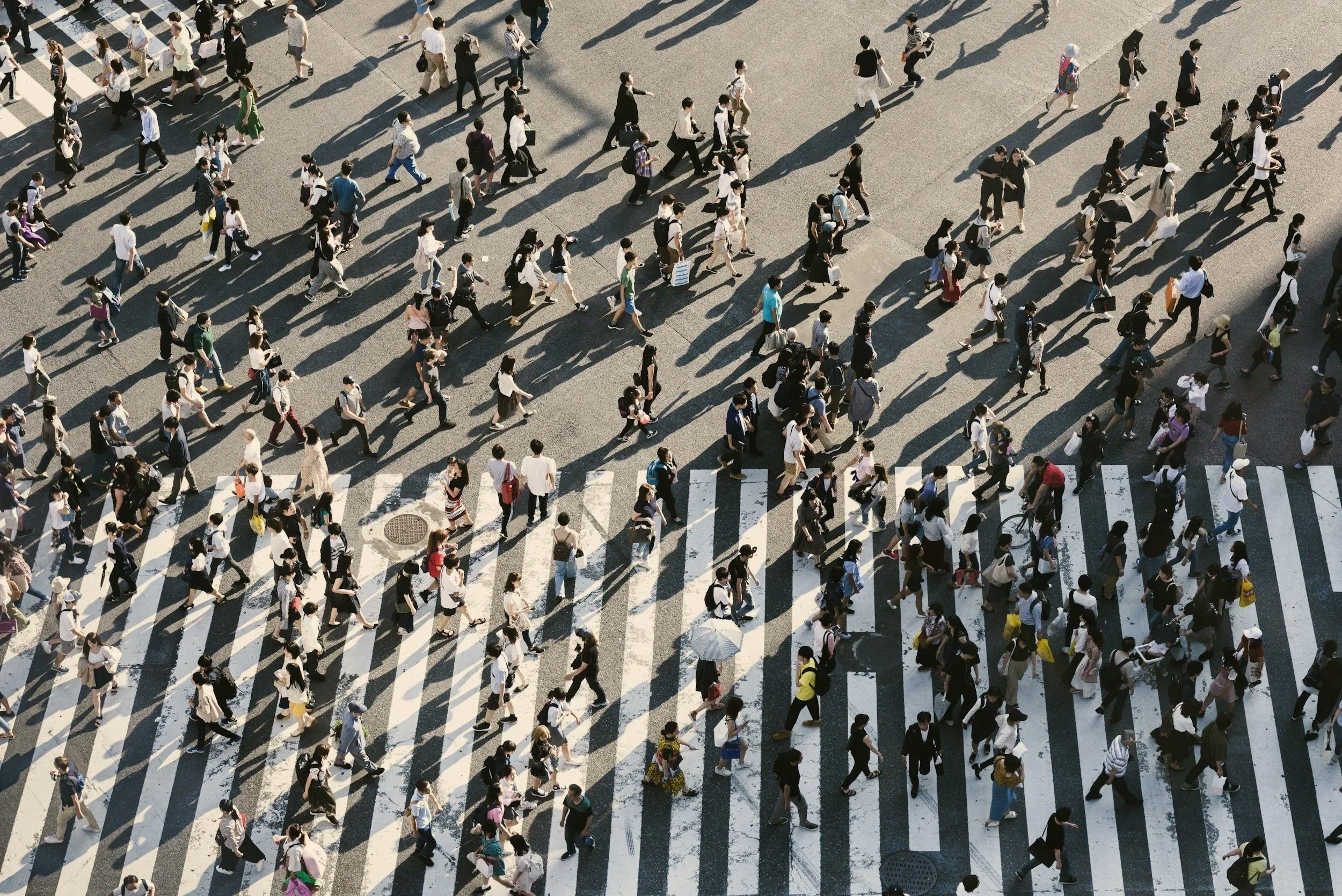 Aerial view of a busy crosswalk filled with pedestrians walking in various directions on a sunny day.