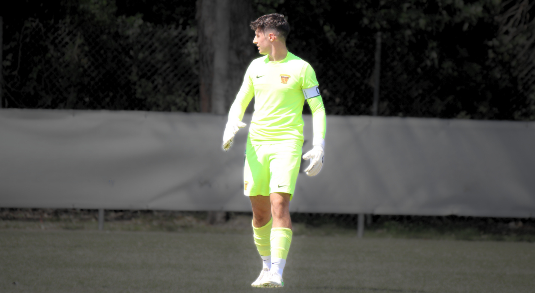 A soccer goalie wearing a bright lime green uniform with a captain's armband standing on a soccer field.